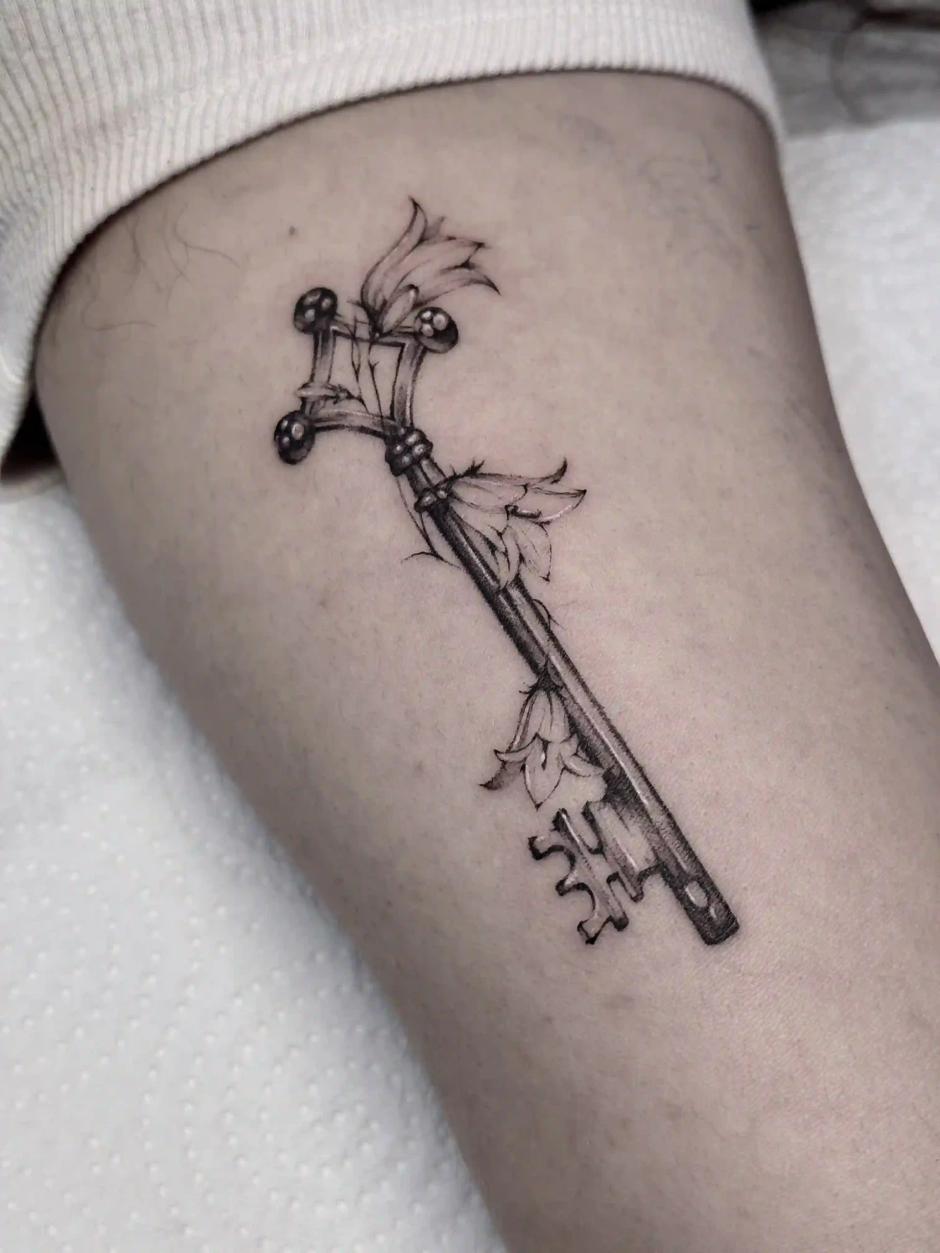 Fineline-Tattoo eines antiken Schlüssels mit Glockenblumen
