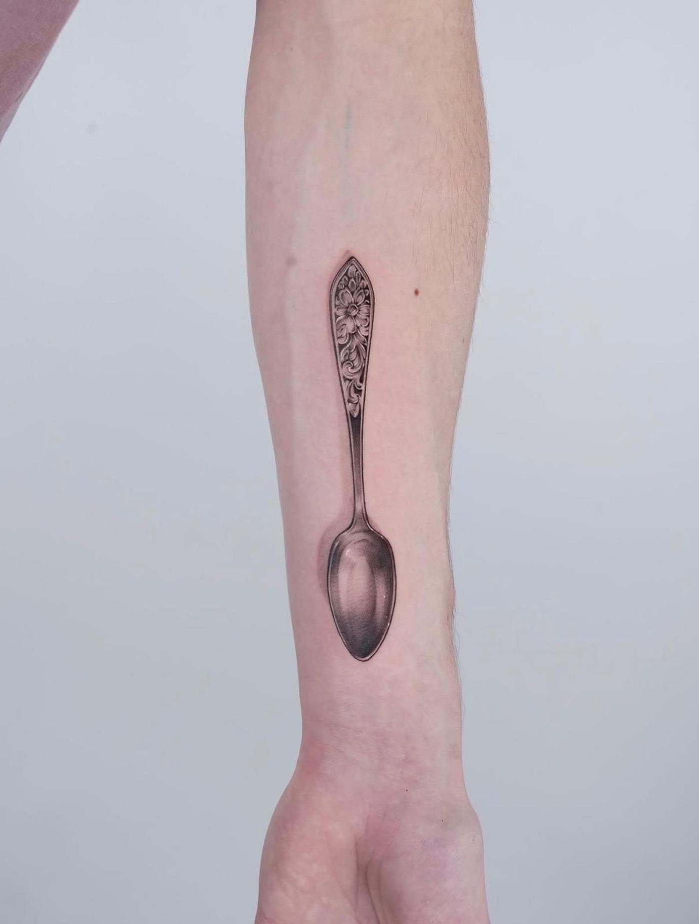 Tattoo am Unterarm: realistisch schattierter Silberlöffel mit floral graviertem Griff