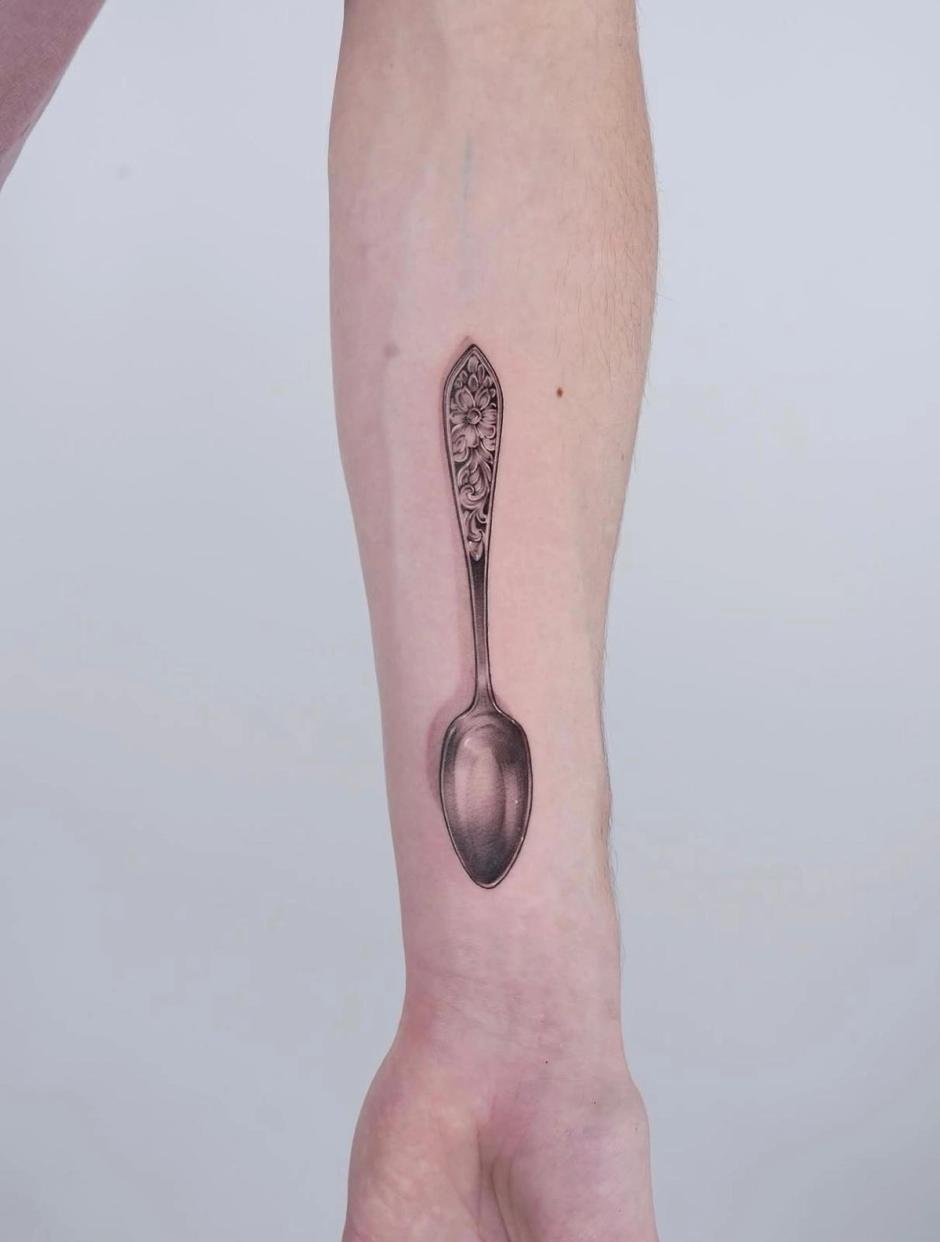 Tattoo am Unterarm: realistisch schattierter Silberlöffel mit floral graviertem Griff