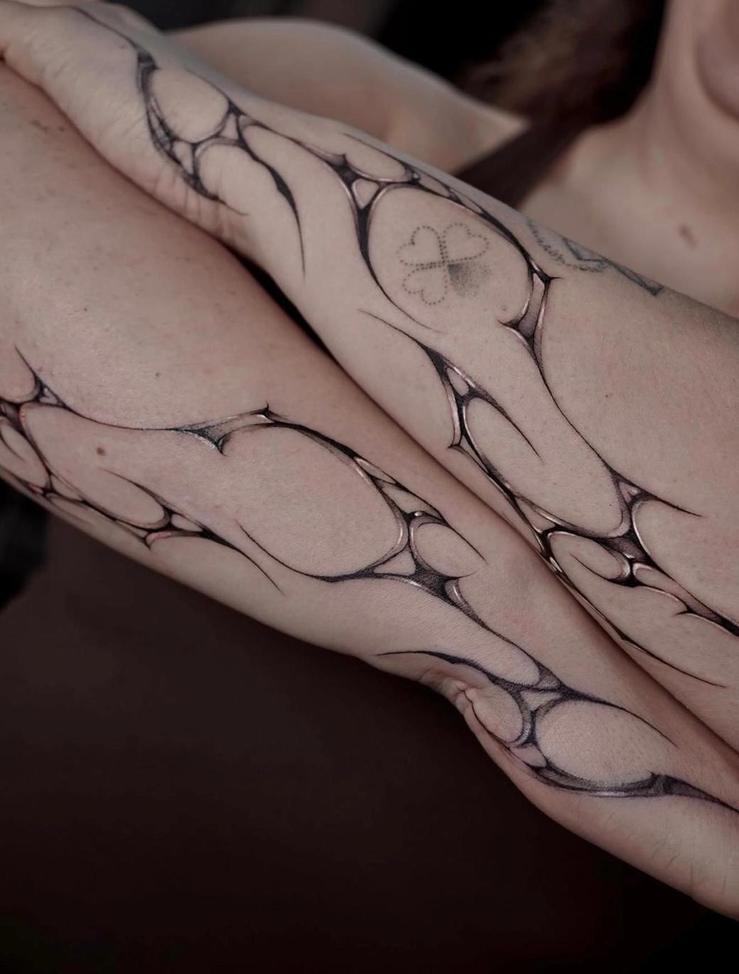 Close-up of the abstract forearm tattoos: flowing, web-like shapes with glossy shading