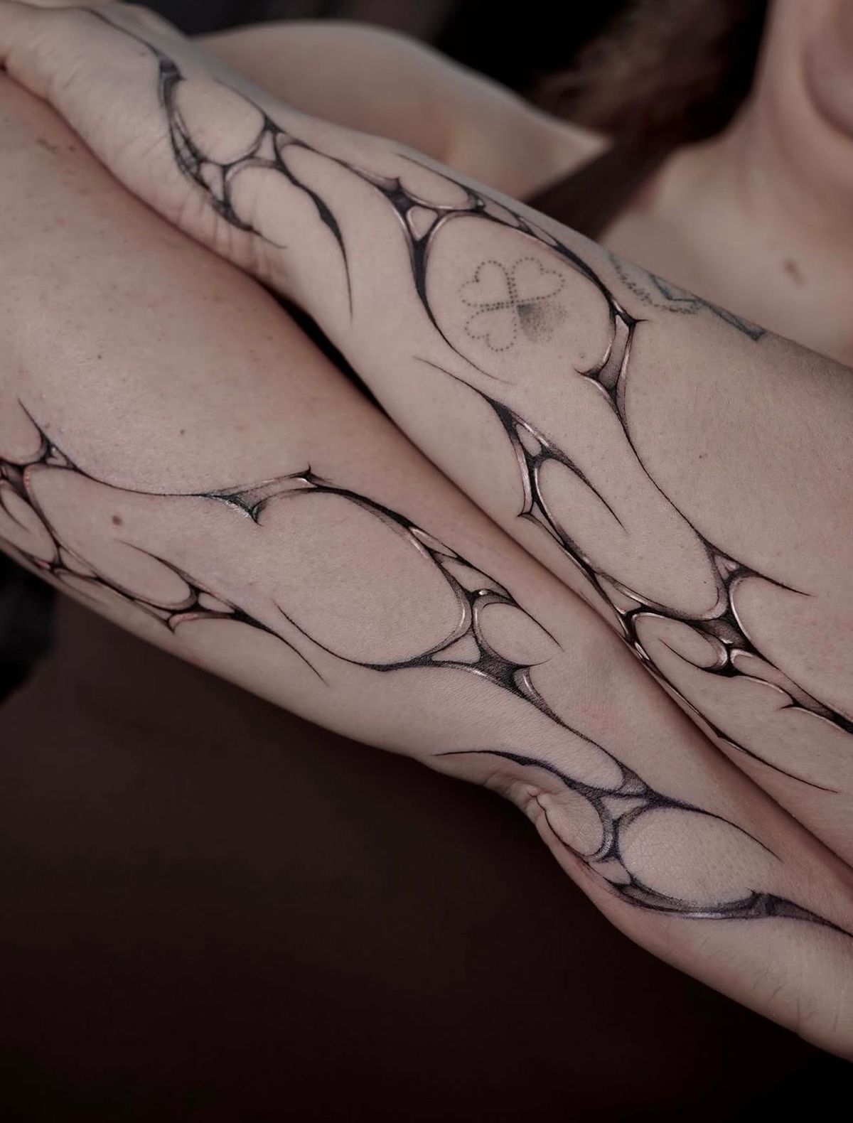 Close-up of the abstract forearm tattoos: flowing, web-like shapes with glossy shading