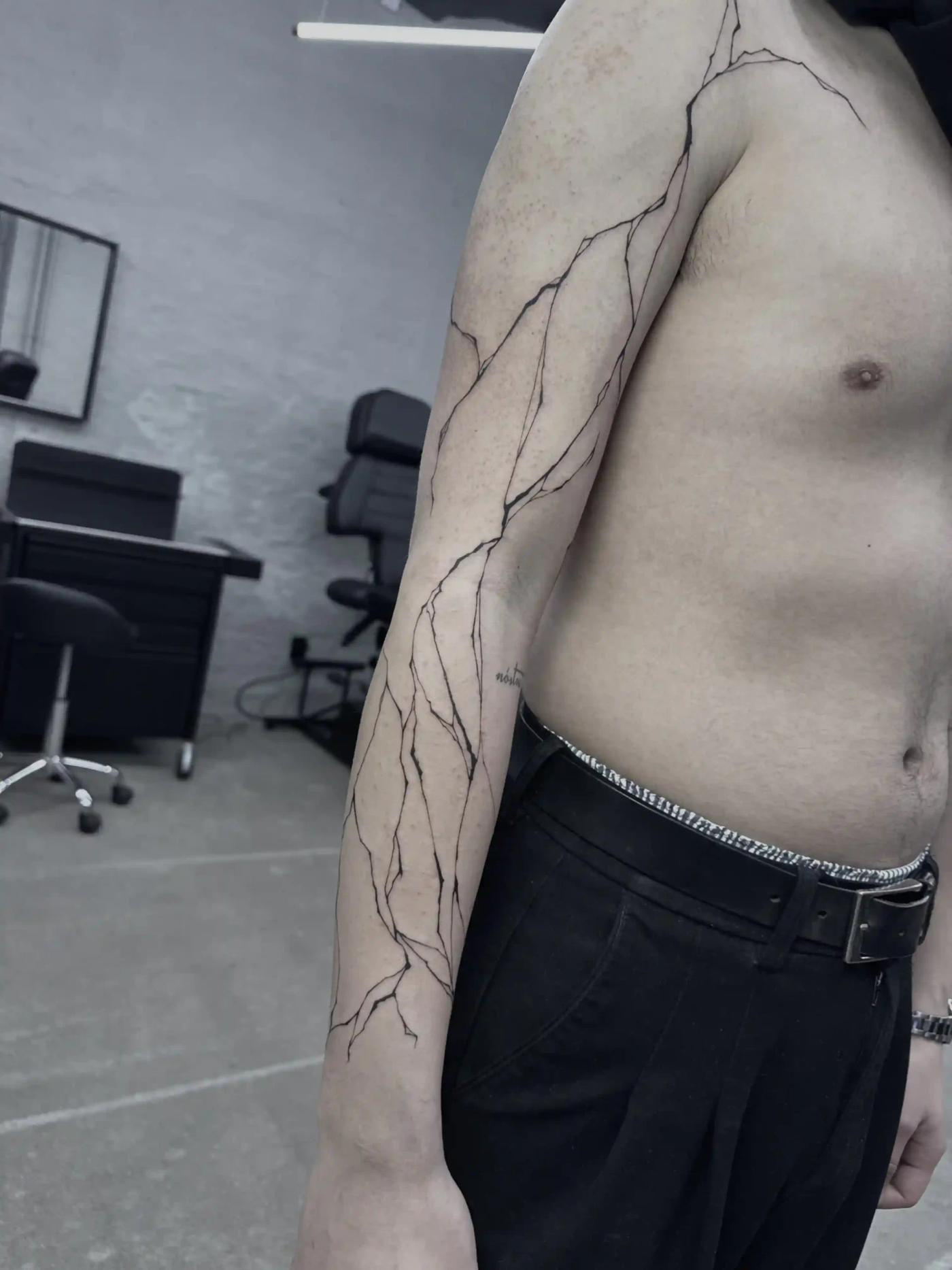 Abstraktes Fineline-Tattoo mit rissartigen Linien über den ganzen Arm