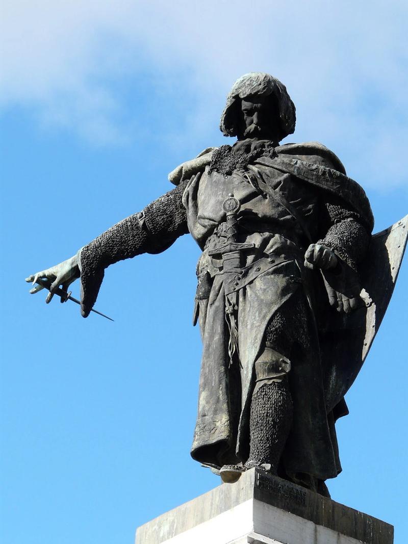 La estatua, en bronce, representa a Guzmán El Bueno sosteniendo con la mano izquierda un escudo, y con la derecha un puñal en actitud de arrojar.