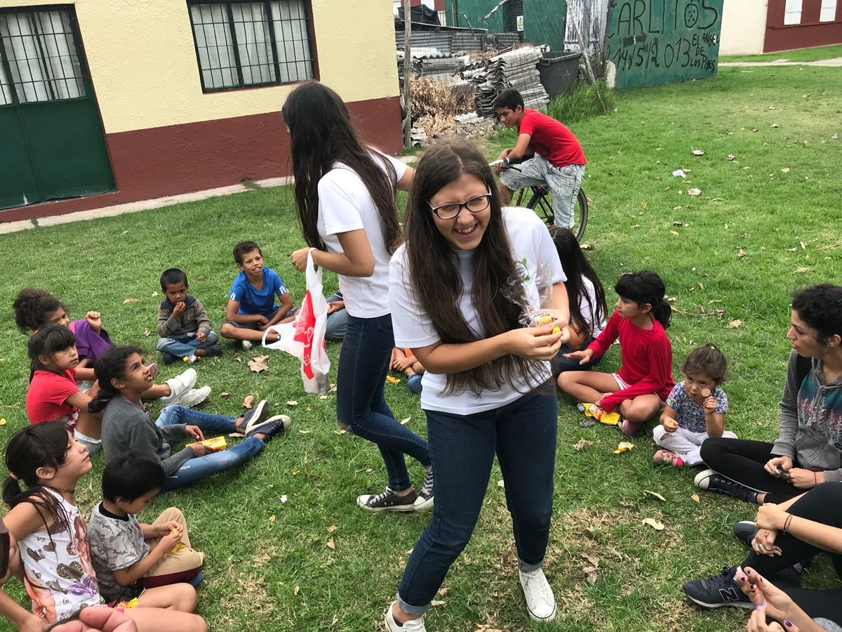 Jóvenes voluntarios reparten golosinas a niños sentados en el césped de un barrio uruguayo.
