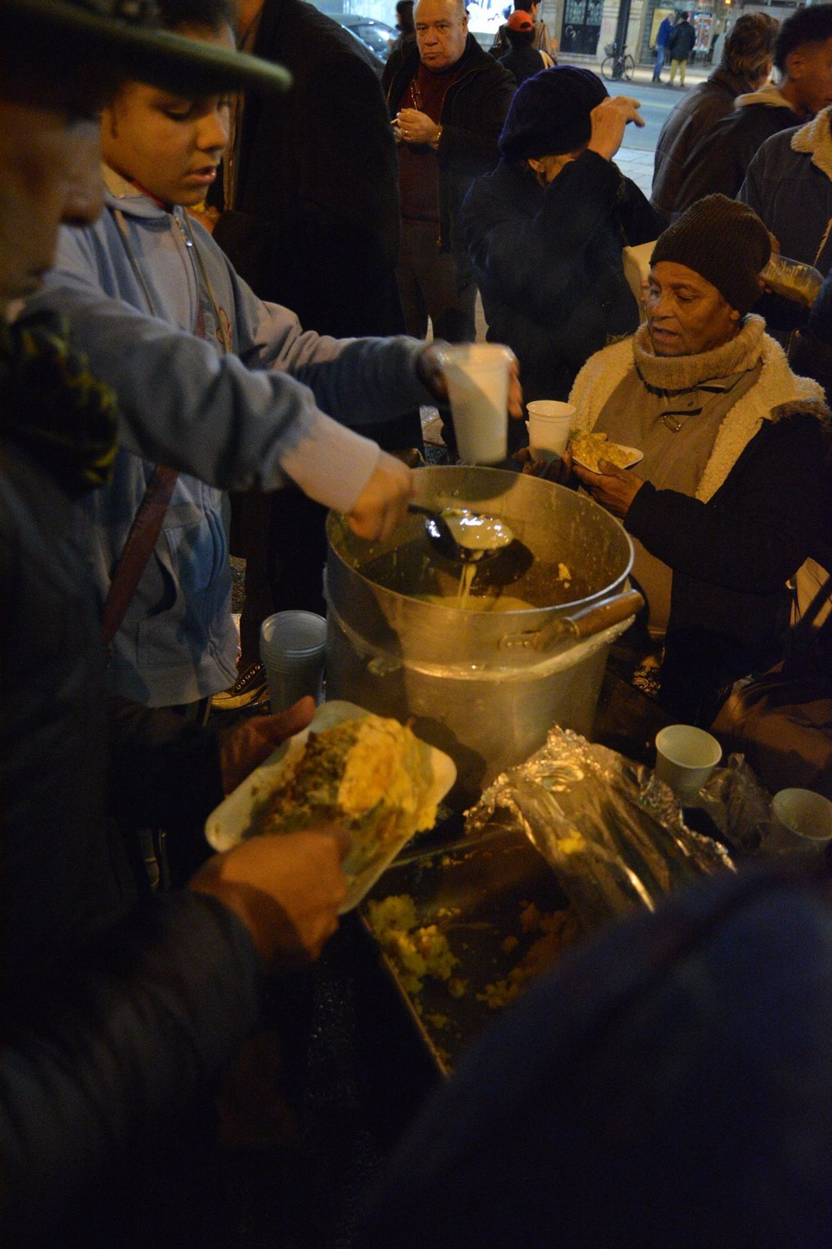 Vecinos sirven comida desde una olla comunitaria a personas en la calle durante la noche en Uruguay.