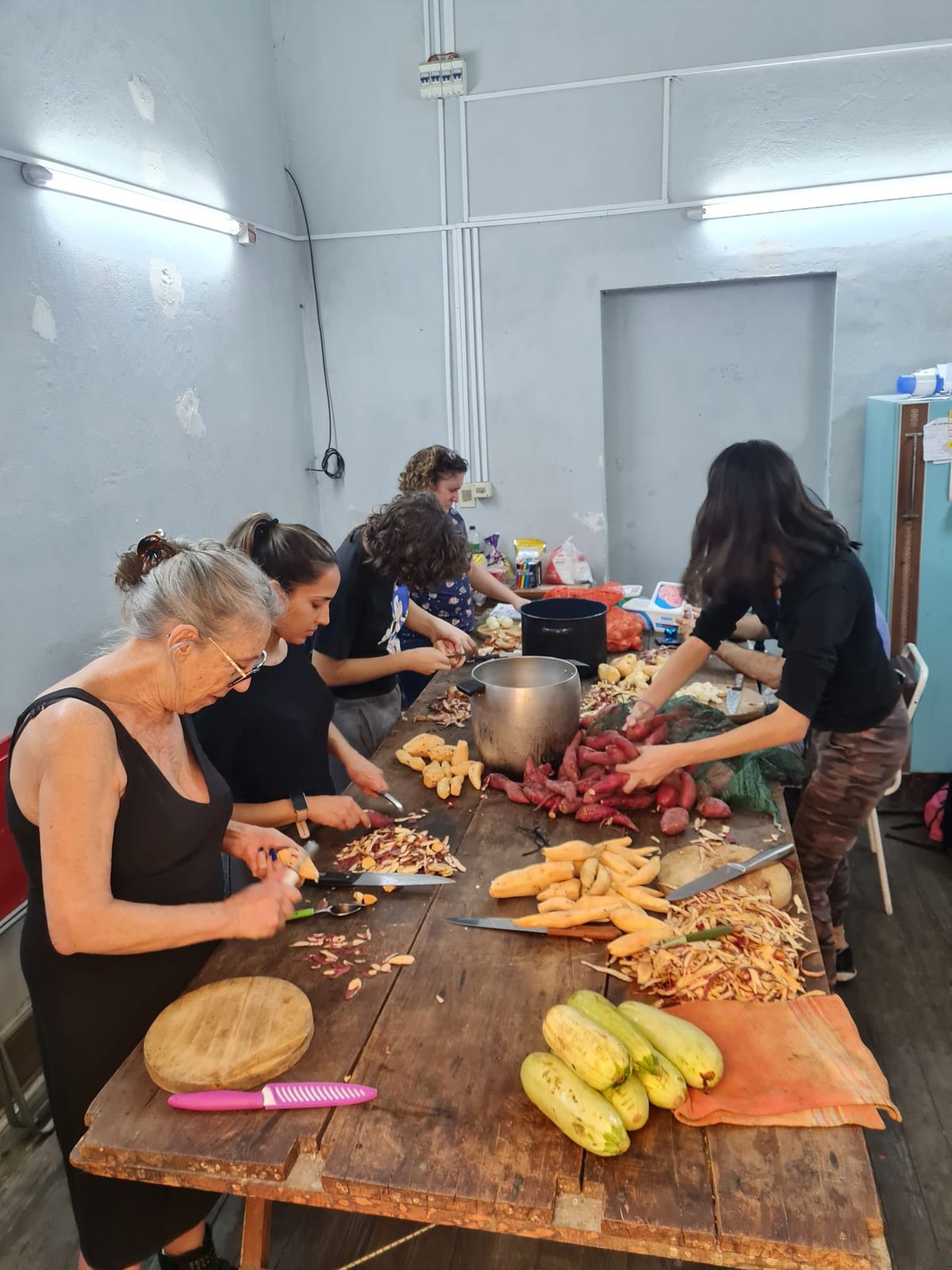 Grupo de voluntarias de distintas generaciones preparando vegetales para una comida comunitaria.