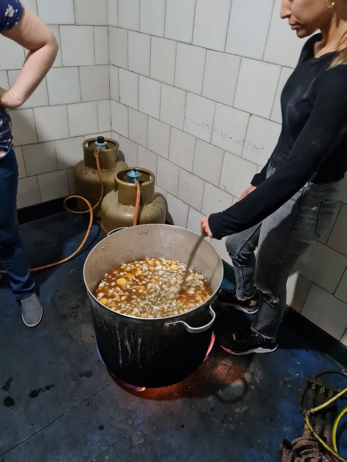 Voluntaria revuelve una olla grande de sopa durante la preparación de una comida comunitaria.