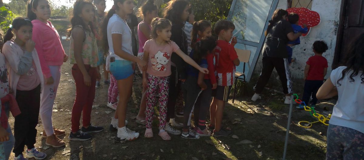 Niños pintando un mural colectivo en una pared de barrio, con la ayuda de una voluntaria.