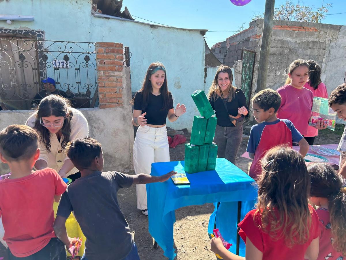 Voluntarias interactúan con niños alrededor de una mesa improvisada en una actividad comunitaria al aire libre en un barrio uruguayo.