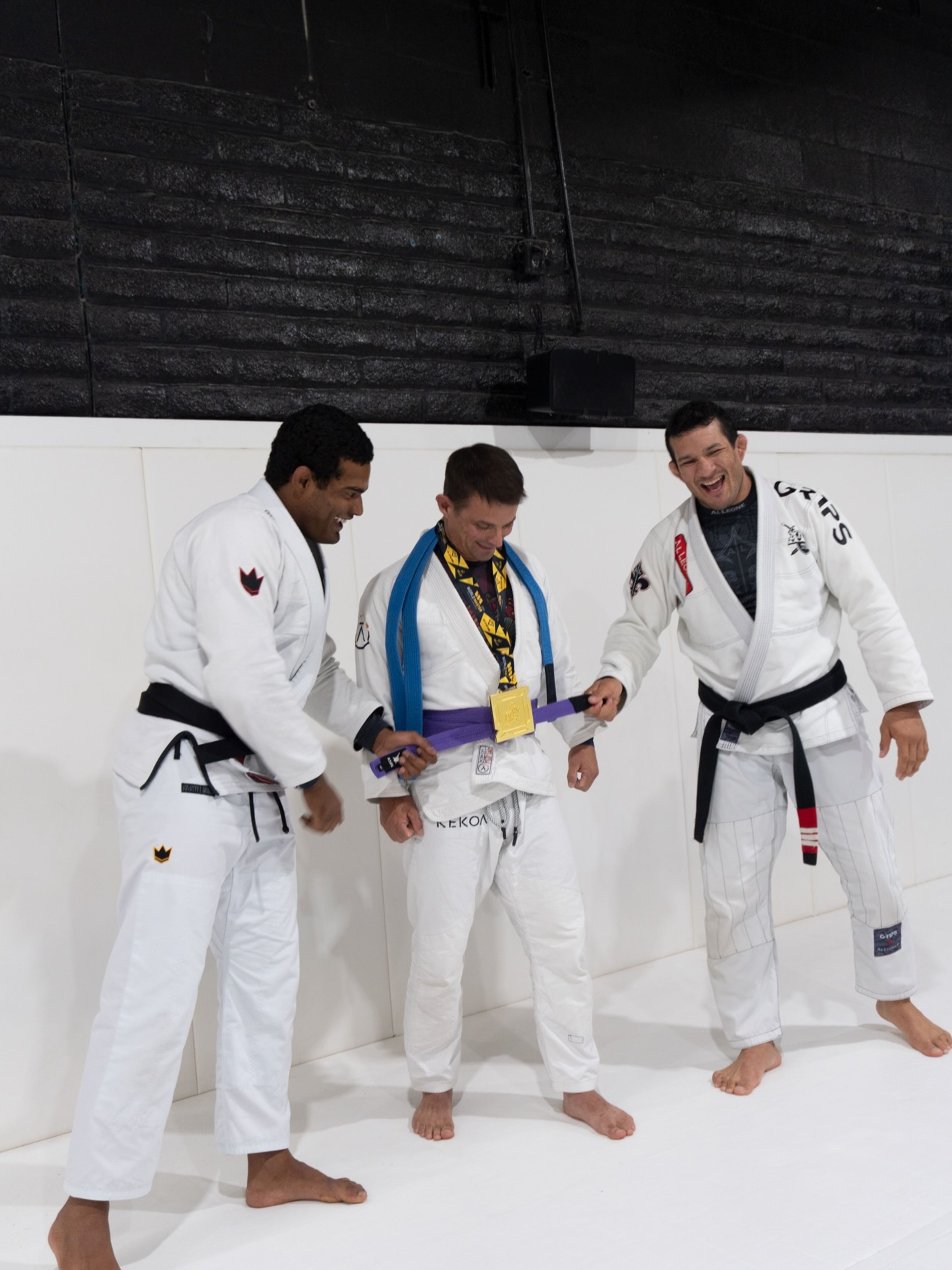 Two coaches tying on a student’s new purple belt