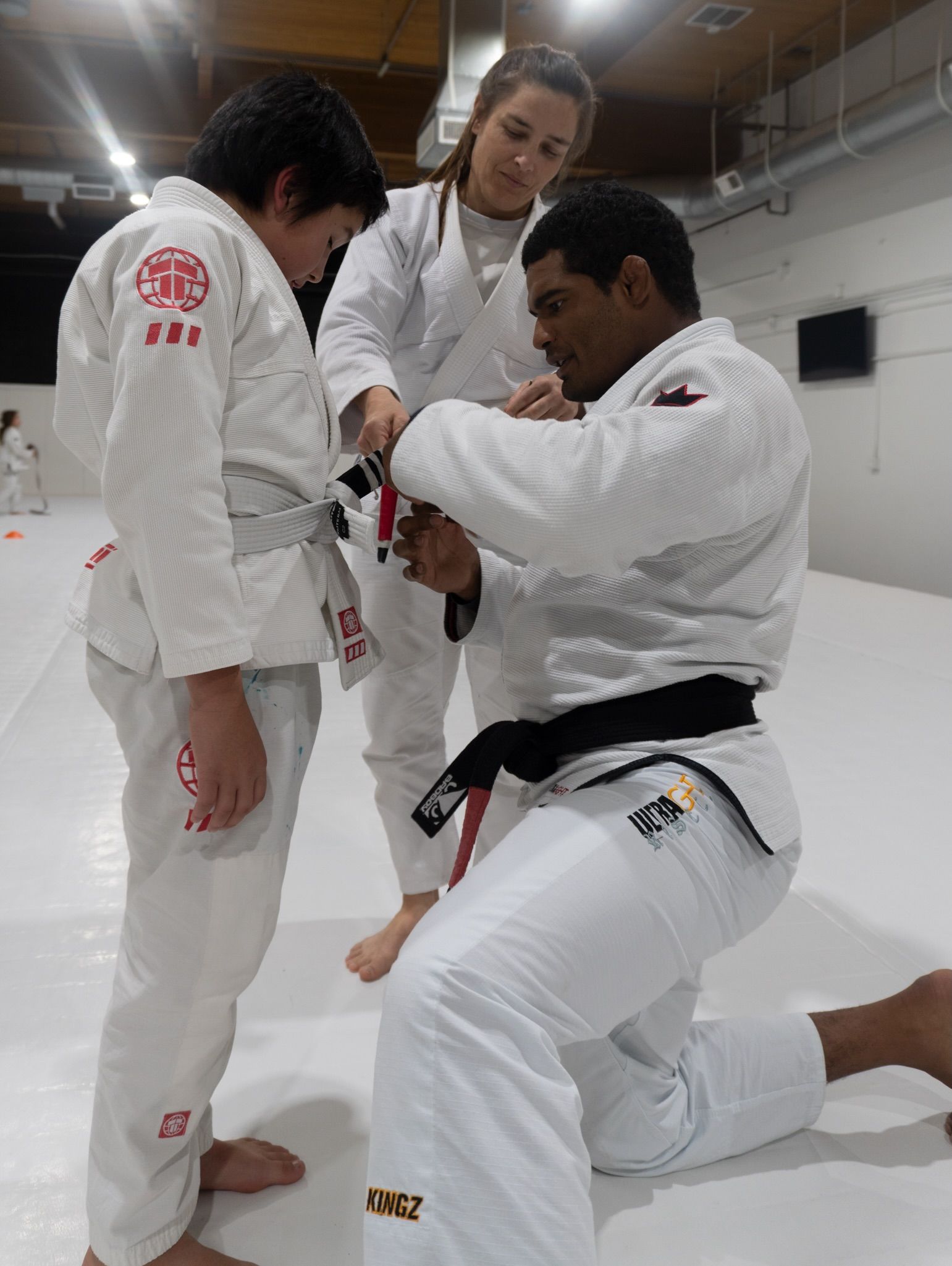 A Pace black belt kneeling to mark a new stripe on a young student’s belt