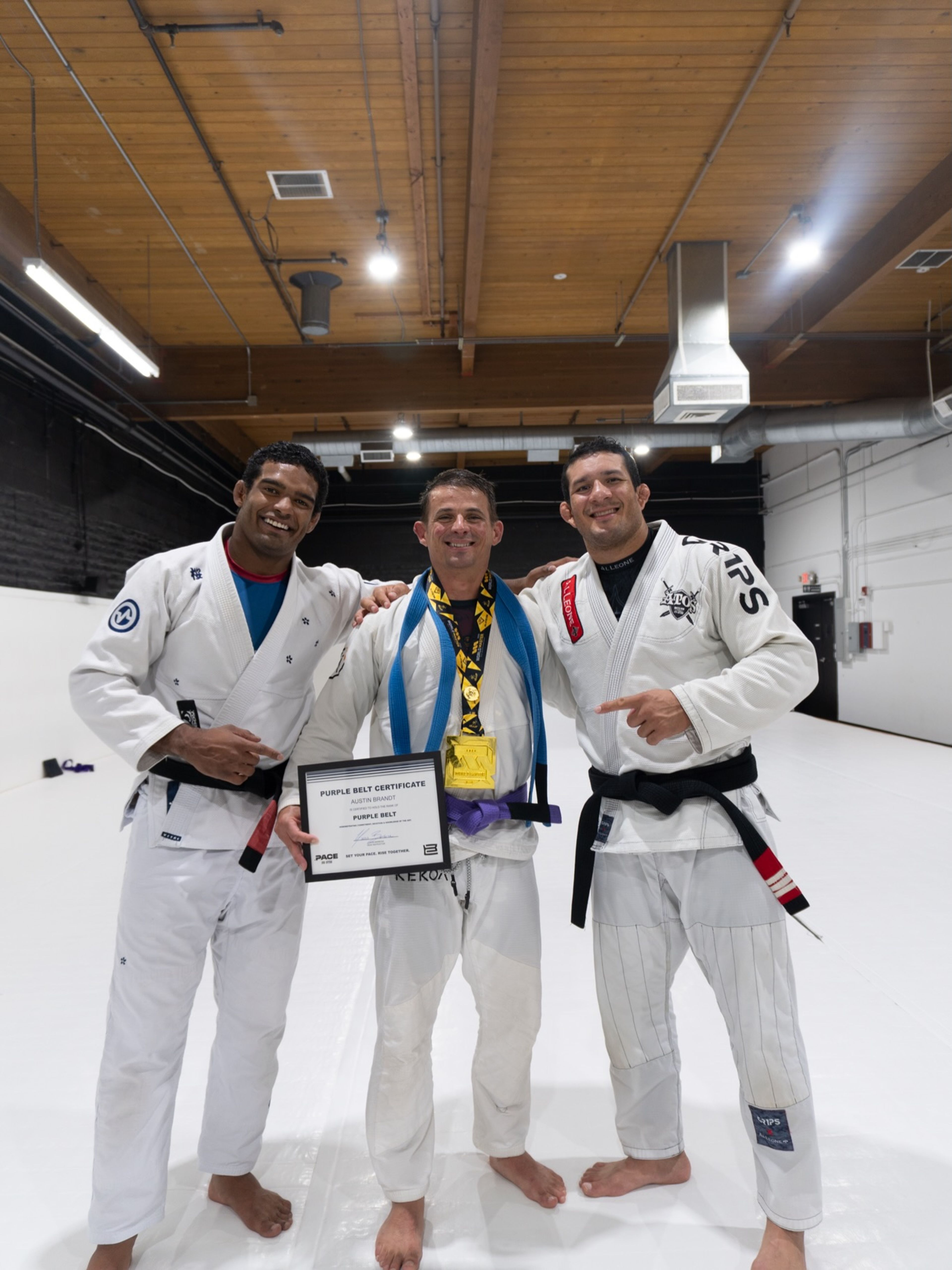 Lucas Barbosa and a Pace black belt either side of a student holding his purple belt certificate
