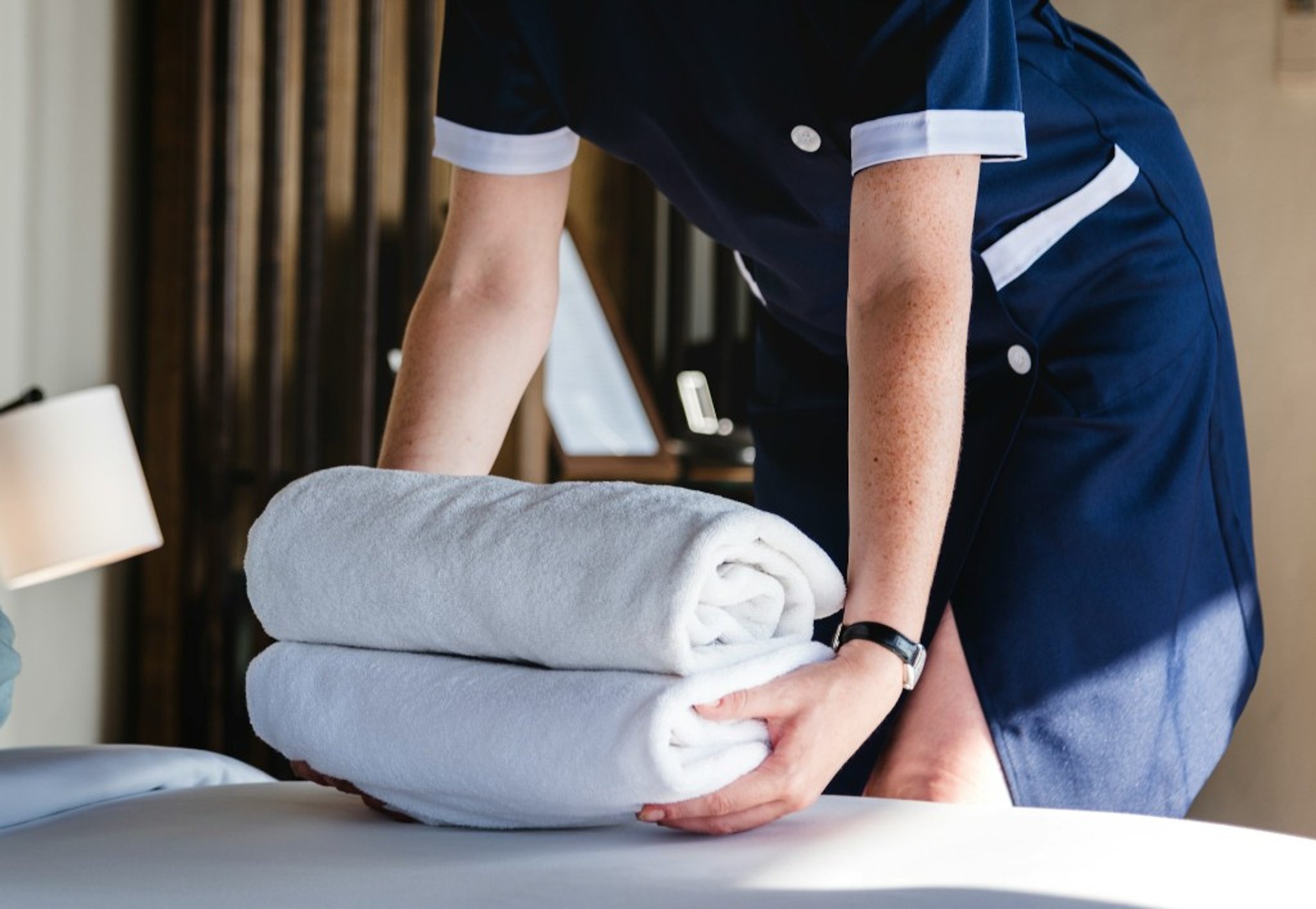 Hotel staff placing fresh white towels on a bed