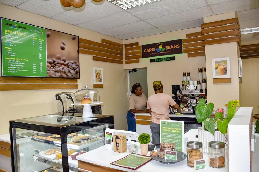 Staff serving customers at the Carib Beans Express coffee counter, with a drinks menu screen and pastry display case