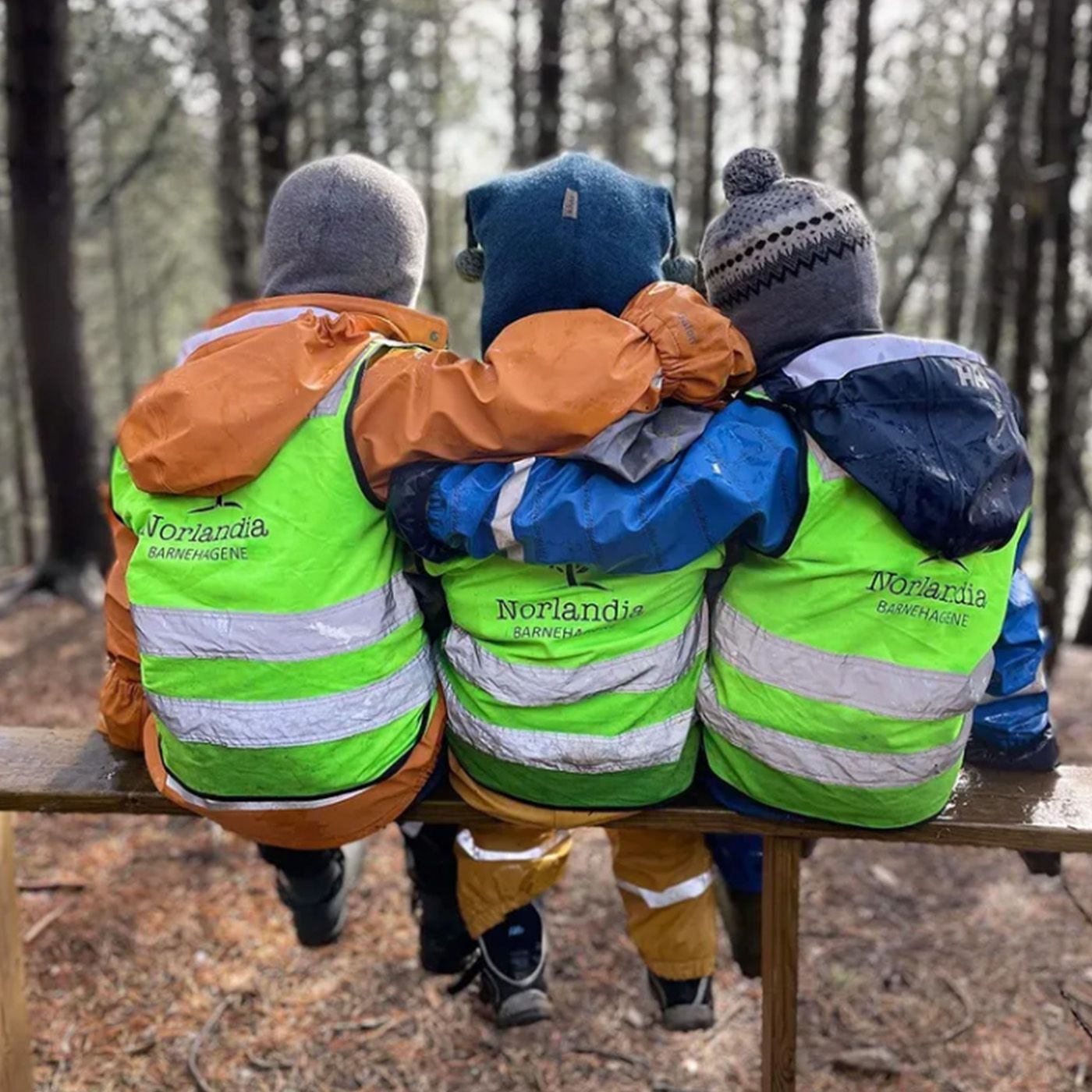 Tre barn sitter og holder rundt hverandre på en benk i skogen