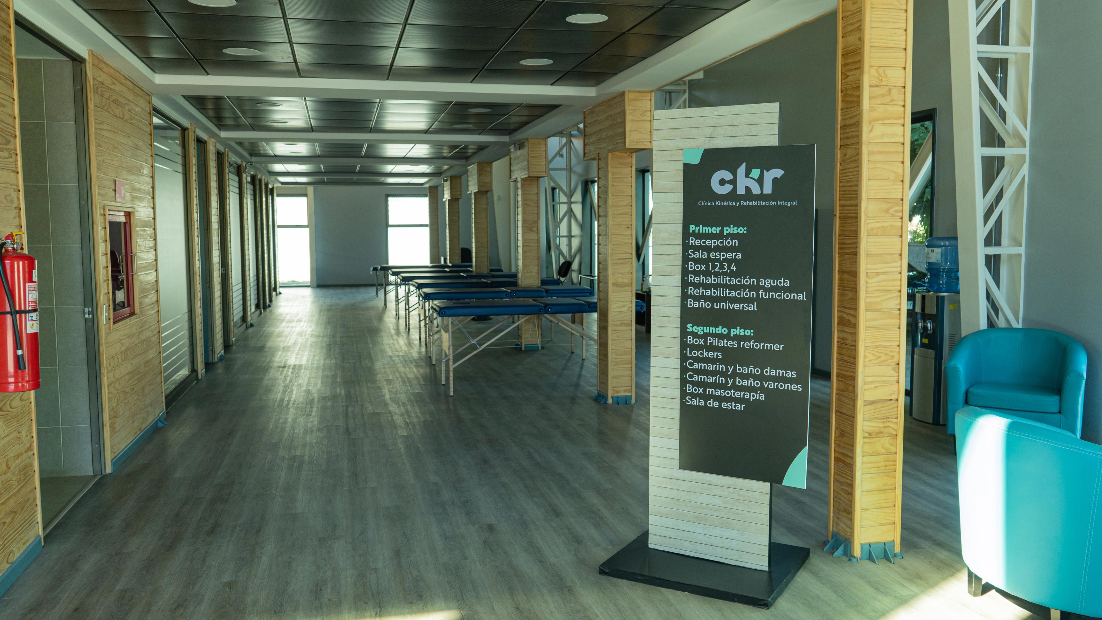 Gimnasio luminoso con suelo de césped artificial verde y luz natural procedente de ventanas altas. Las máquinas de ejercicio y las estanterías con pesas se alinean a lo largo de las paredes.