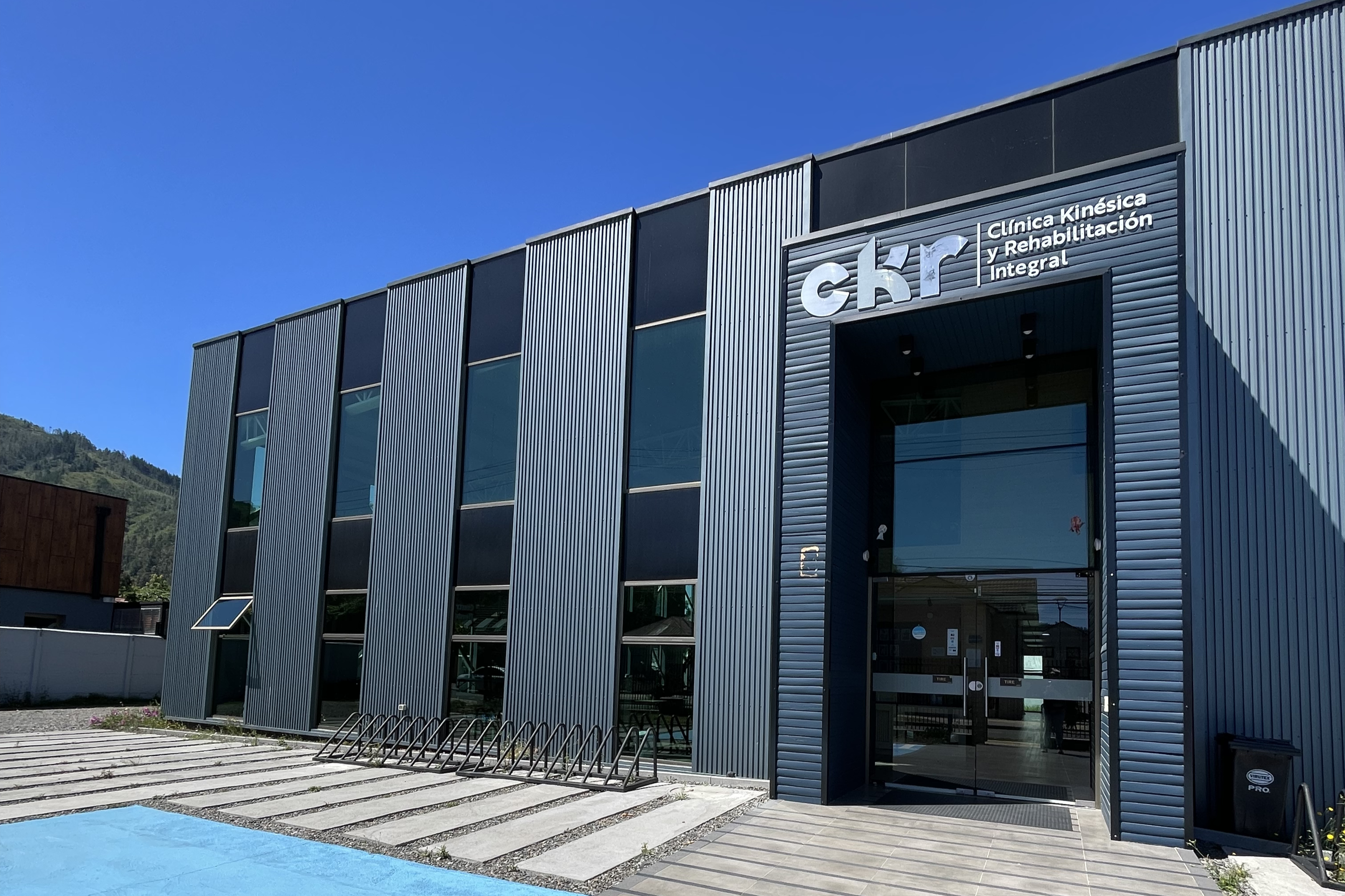 Edificio moderno de dos plantas de CKR con ventanas verticales y fachada ondulada bajo un cielo azul claro.