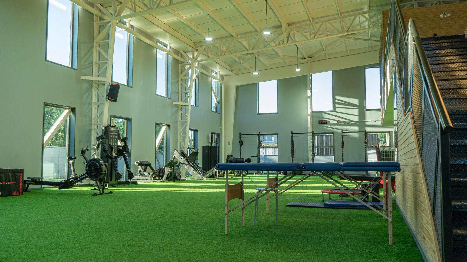 Gimnasio espacioso con máquinas de remo y pesas. Ambiente luminoso y aireado.