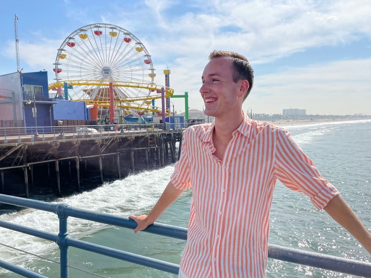 A casual photo of Thomas smiling with Santa Monica's Ferris wheel in the background on a sunny day.