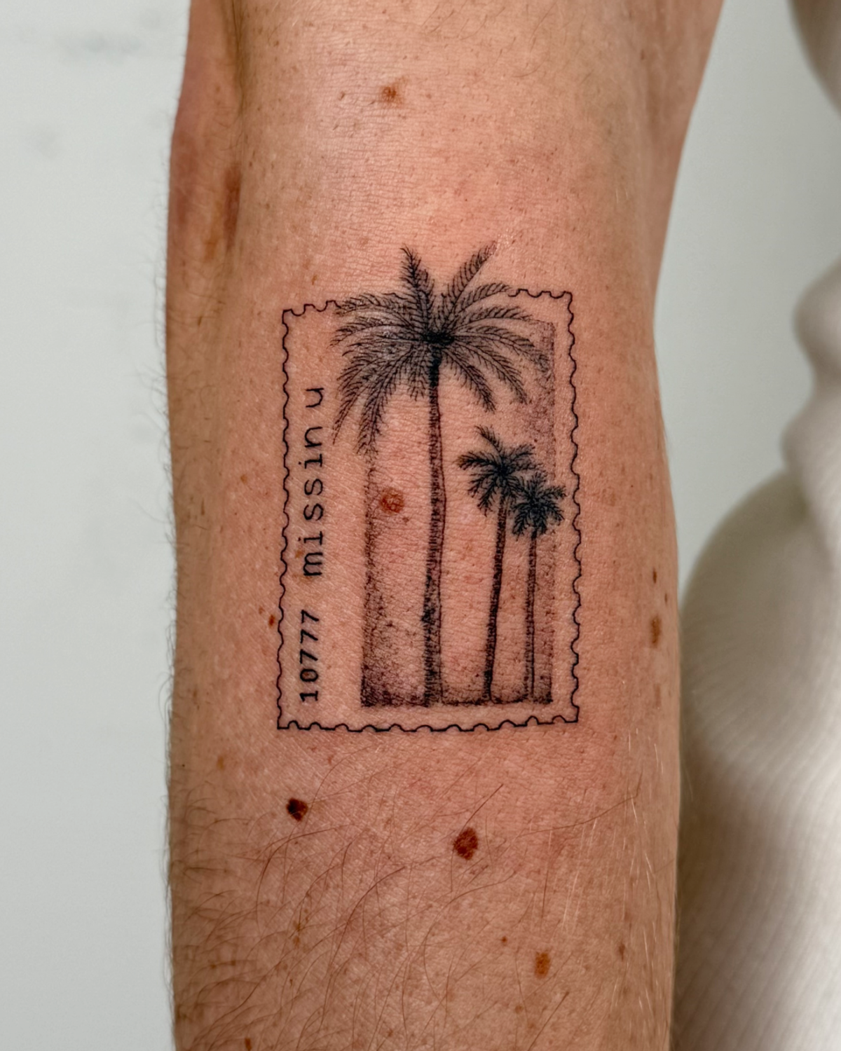 A photo of Thomas' tattoo, a black and white illustration of a postage stamp with LA's iconic palm trees, with TORI's lead single "Missin U" text next to it.