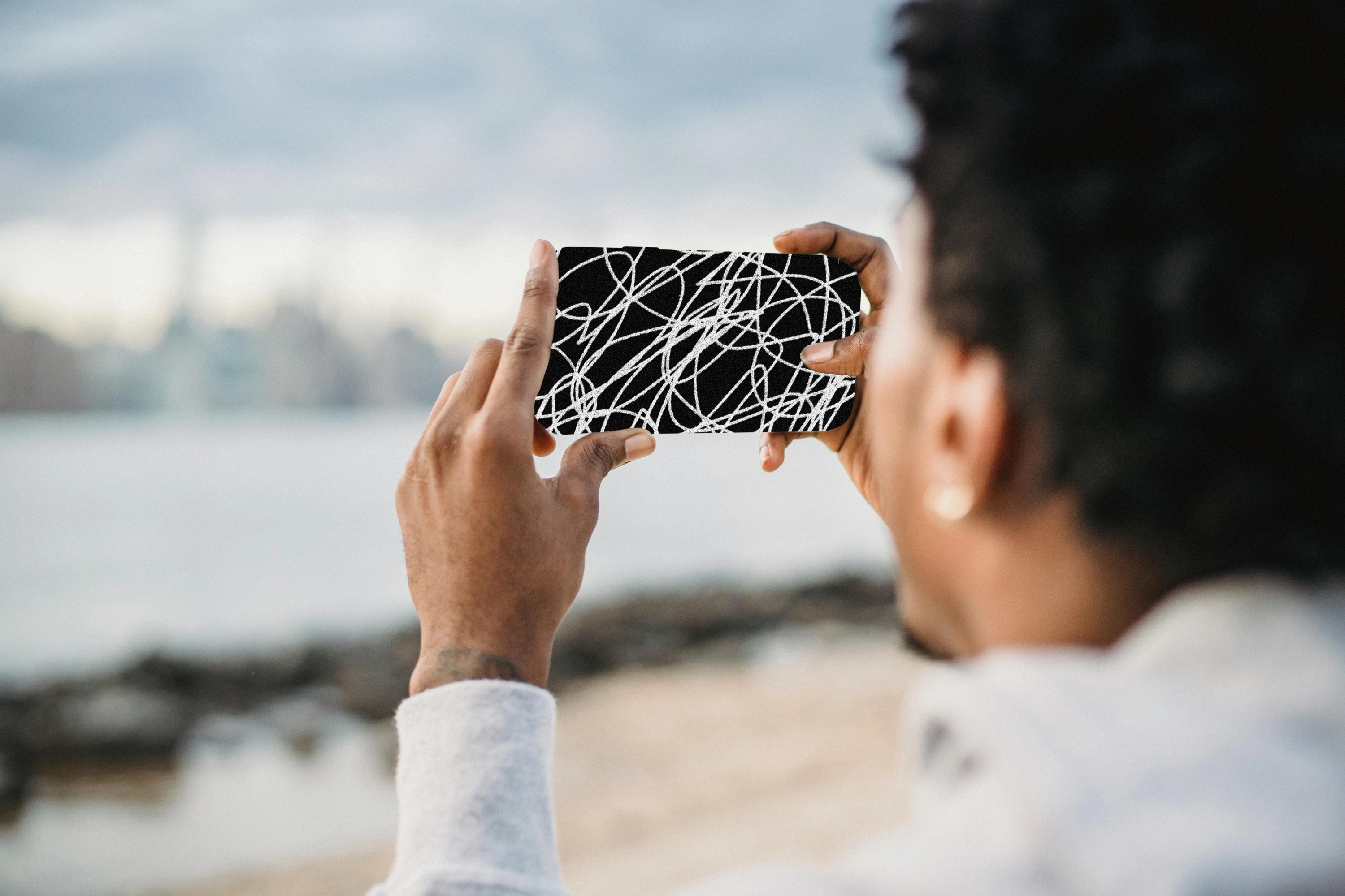 Blurred-out person holding a scribbled out phone, taking a photo of a city skylin