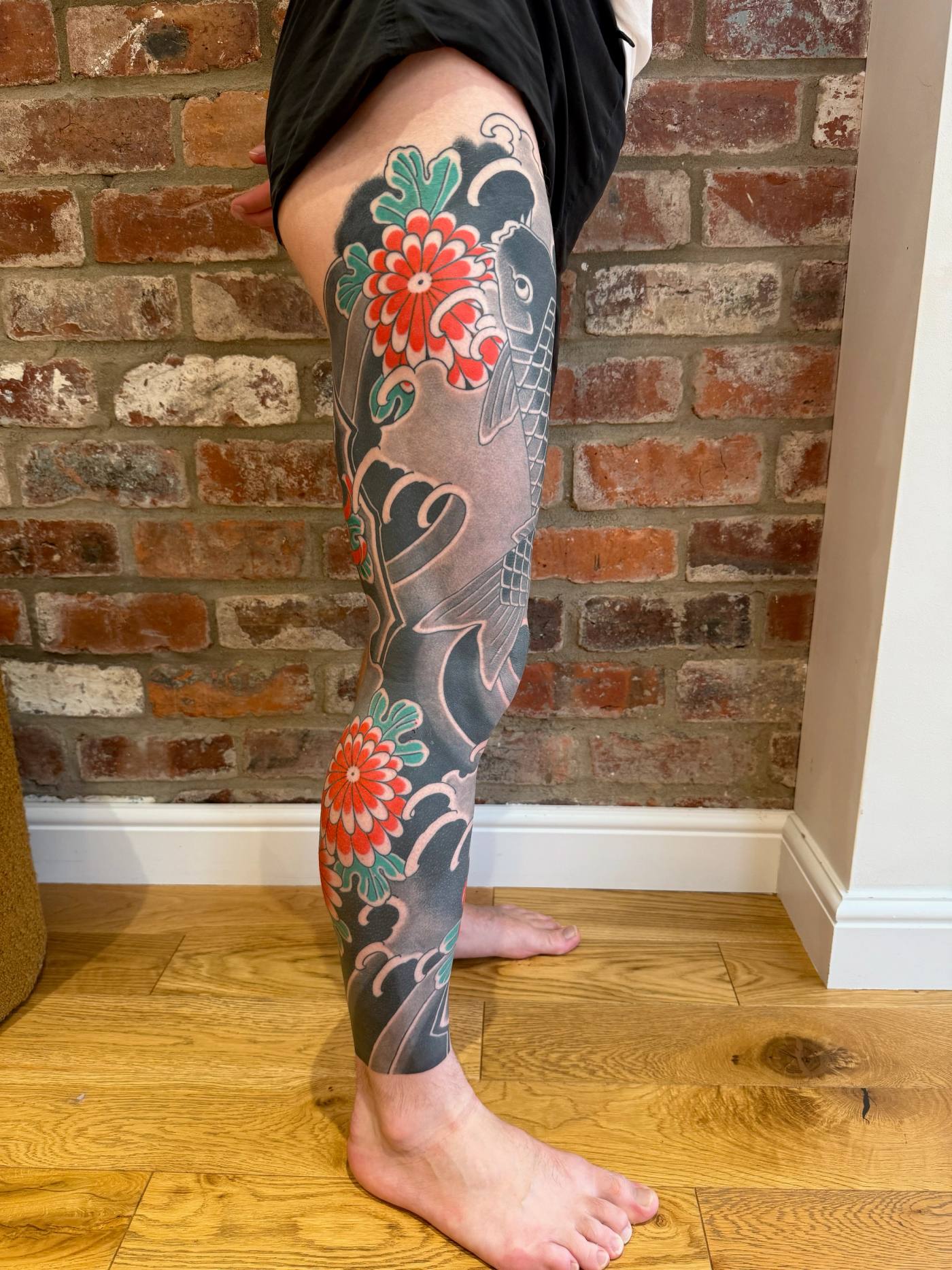 The finished right leg sleeve from the side: koi, waves and red chrysanthemums against the black background