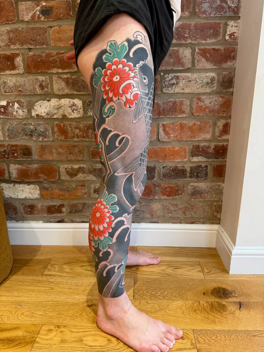 The finished right leg sleeve from the side: koi, waves and red chrysanthemums against the black background