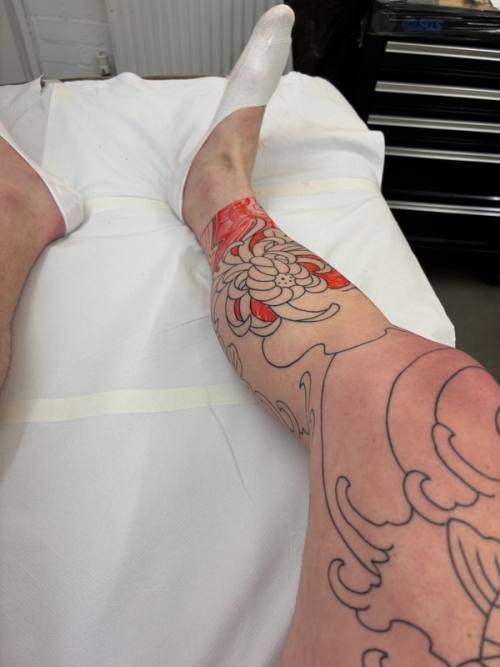 Right foot on the table with the chrysanthemum stencil on the shin, before the shading begins