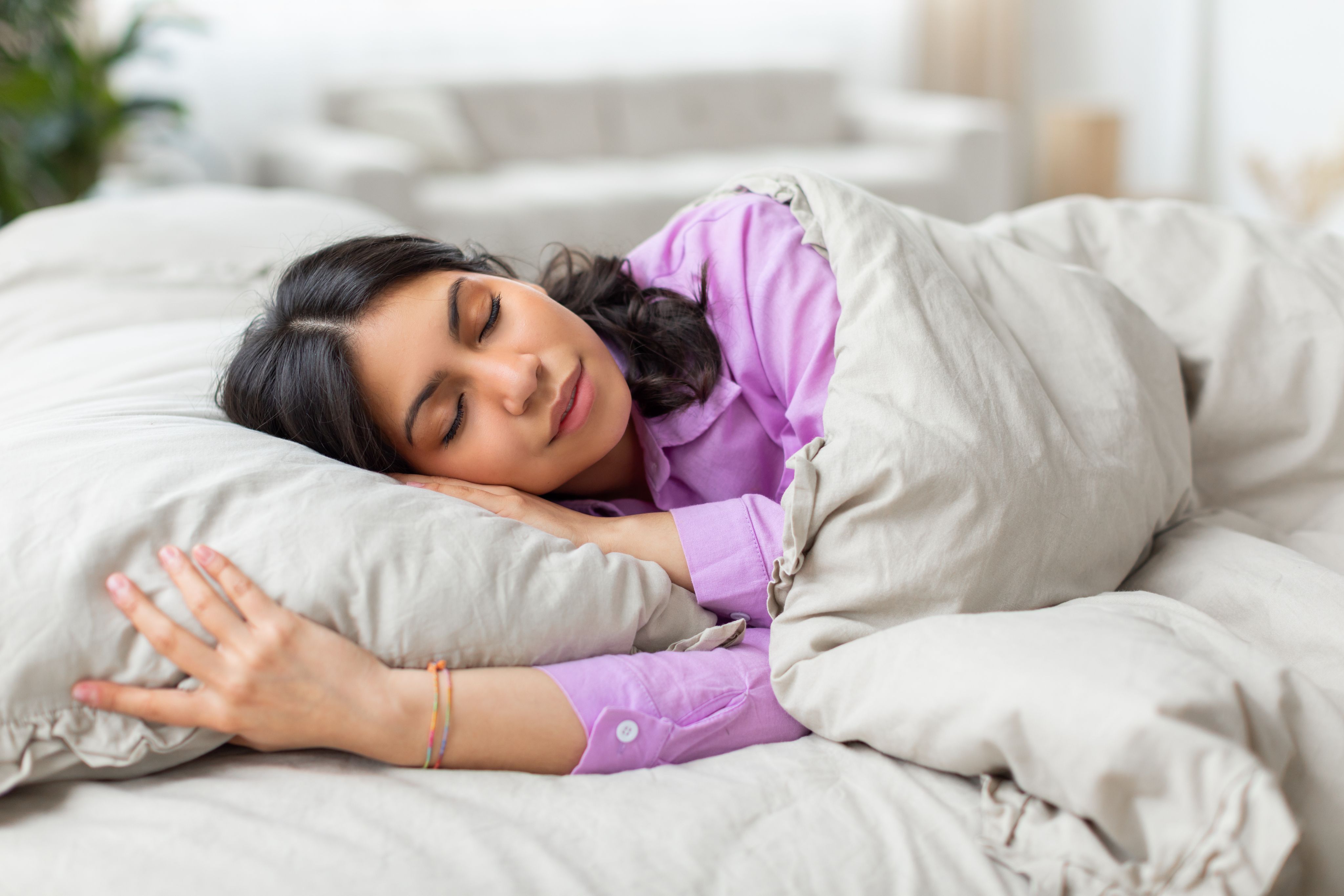 Woman sleeping peacefully in a comfortable bed, demonstrating healthy sleep habits, rest, recovery, and overall wellness in a bright bedroom environment