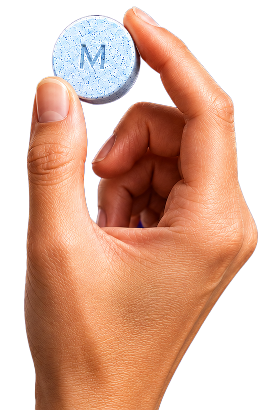 Hand holding a blue speckled wellness tablet with an embossed M logo, isolated on a transparent background, representing premium nutritional supplementation, daily health support, and convenient wellness solutions.