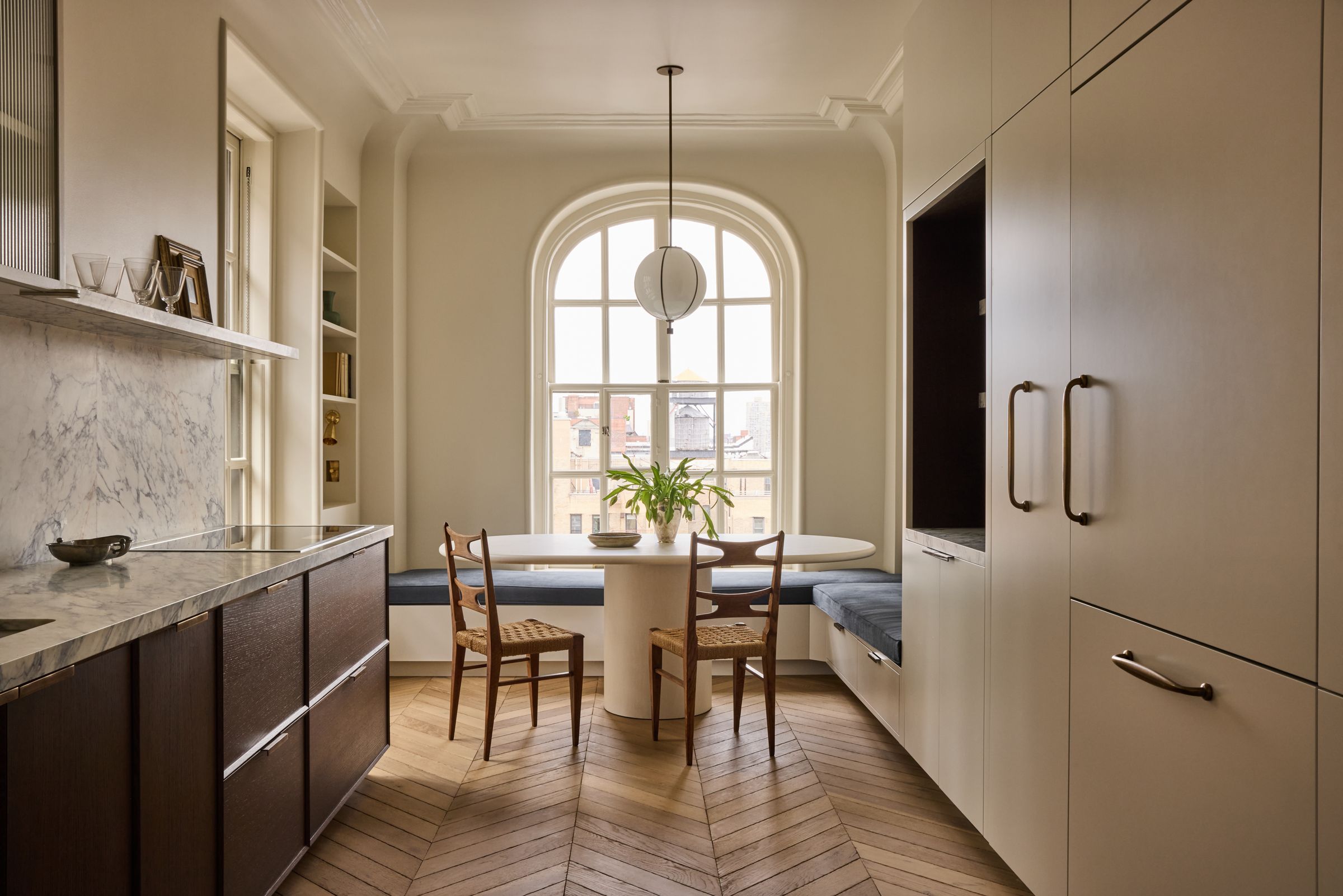 A kitchen dining nook with a built-in bench and an oval table set before a large arched window with a pendant light.