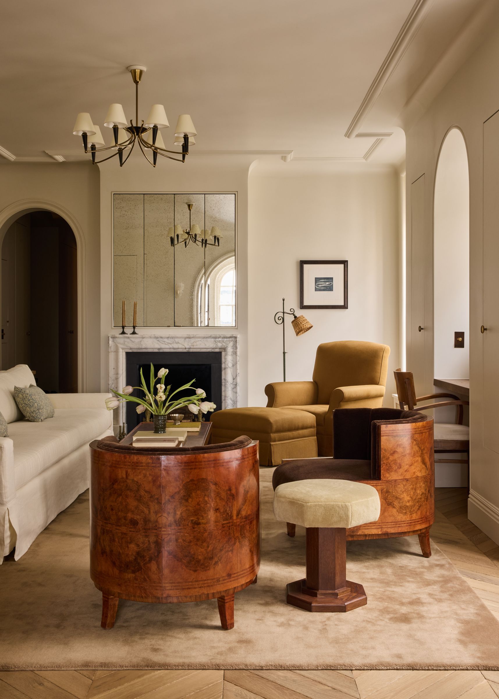An elegant living room featuring two large, rounded burl wood armchairs, a mustard armchair, and a marble fireplace.