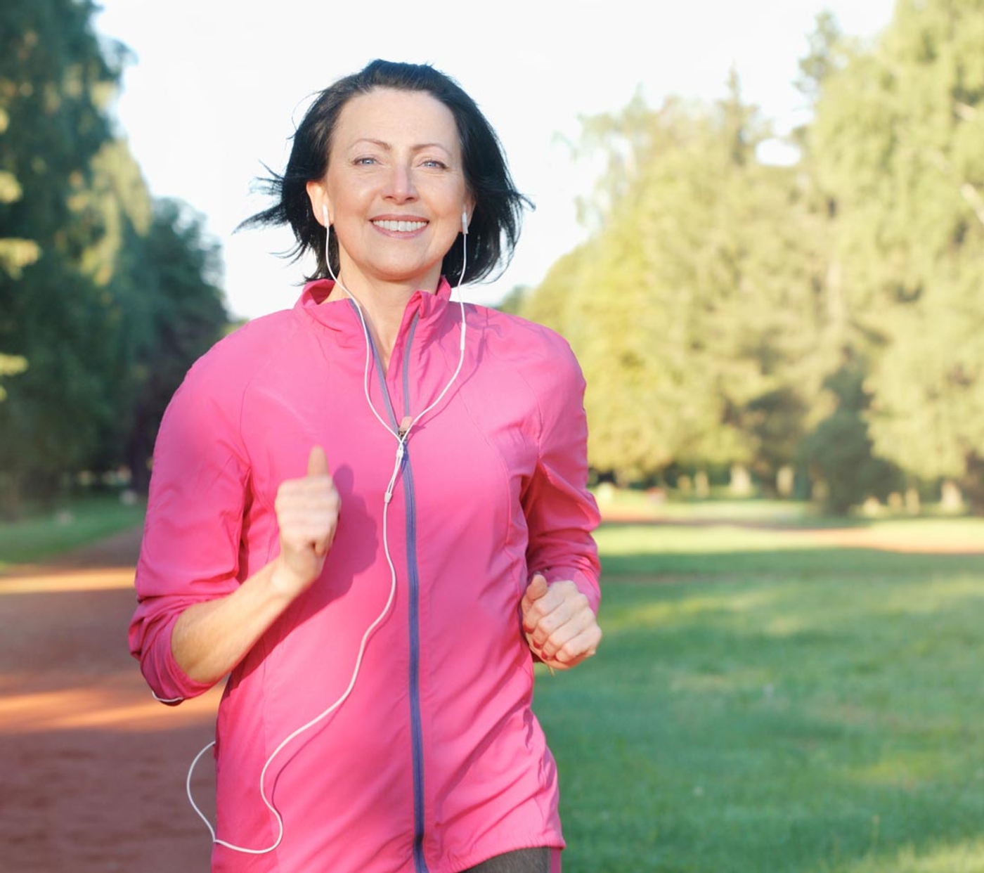 Woman in pink jacket running in the park listening to music through her wired headphones