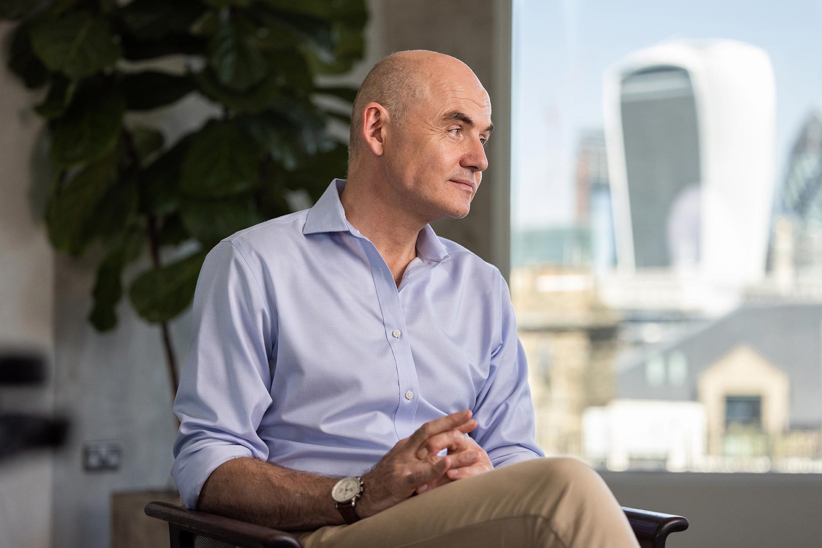 Mr Paul Harris wearing a blue shirt, sitting in a chair, with London skyline backdrop