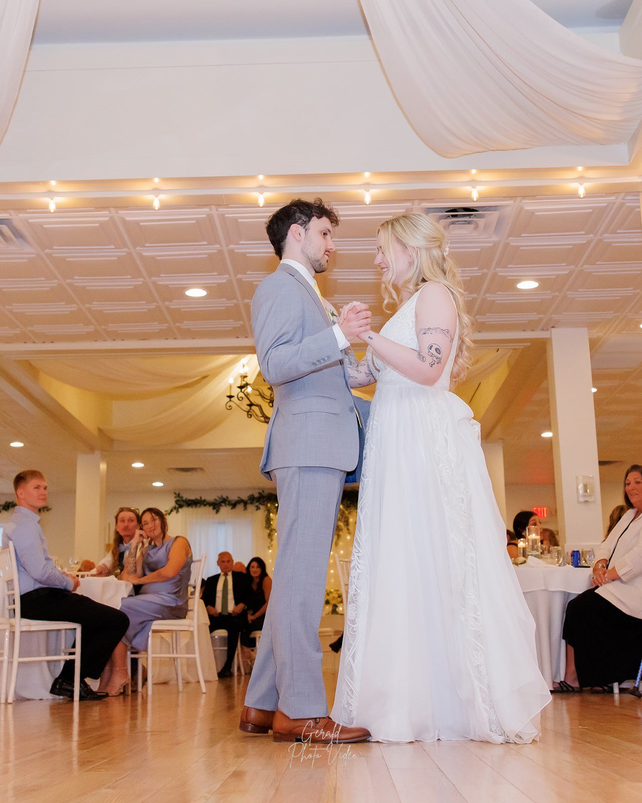 Logan and John sharing their first dance under draped ceiling fabric and a chandelier at The Arbor Event Venue