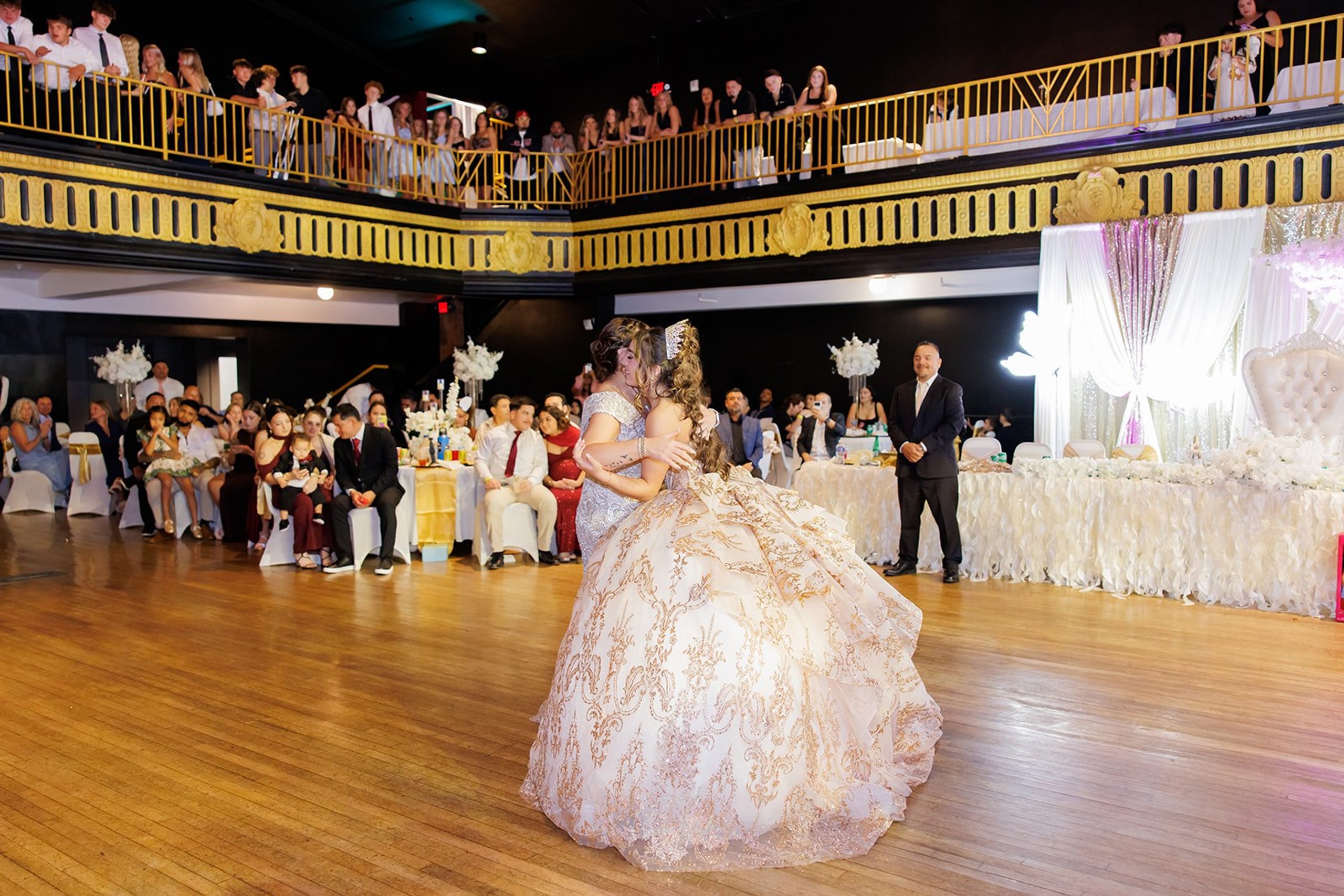 Vista amplia de Sophia bailando con su mamá mientras los invitados miran desde las mesas y el balcón en Admiral Theater, Omaha
