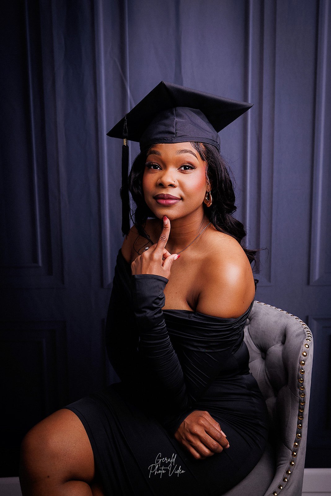 Graduate in a cap and black off-shoulder dress seated in a studio, Nebraska graduation portrait