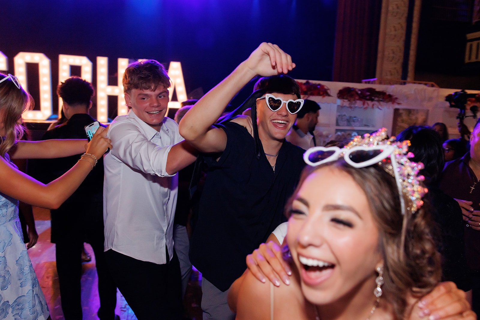 Sophia riendo con lentes de sol en forma de corazón mientras sus invitados bailan a su alrededor en su quinceañera en Omaha