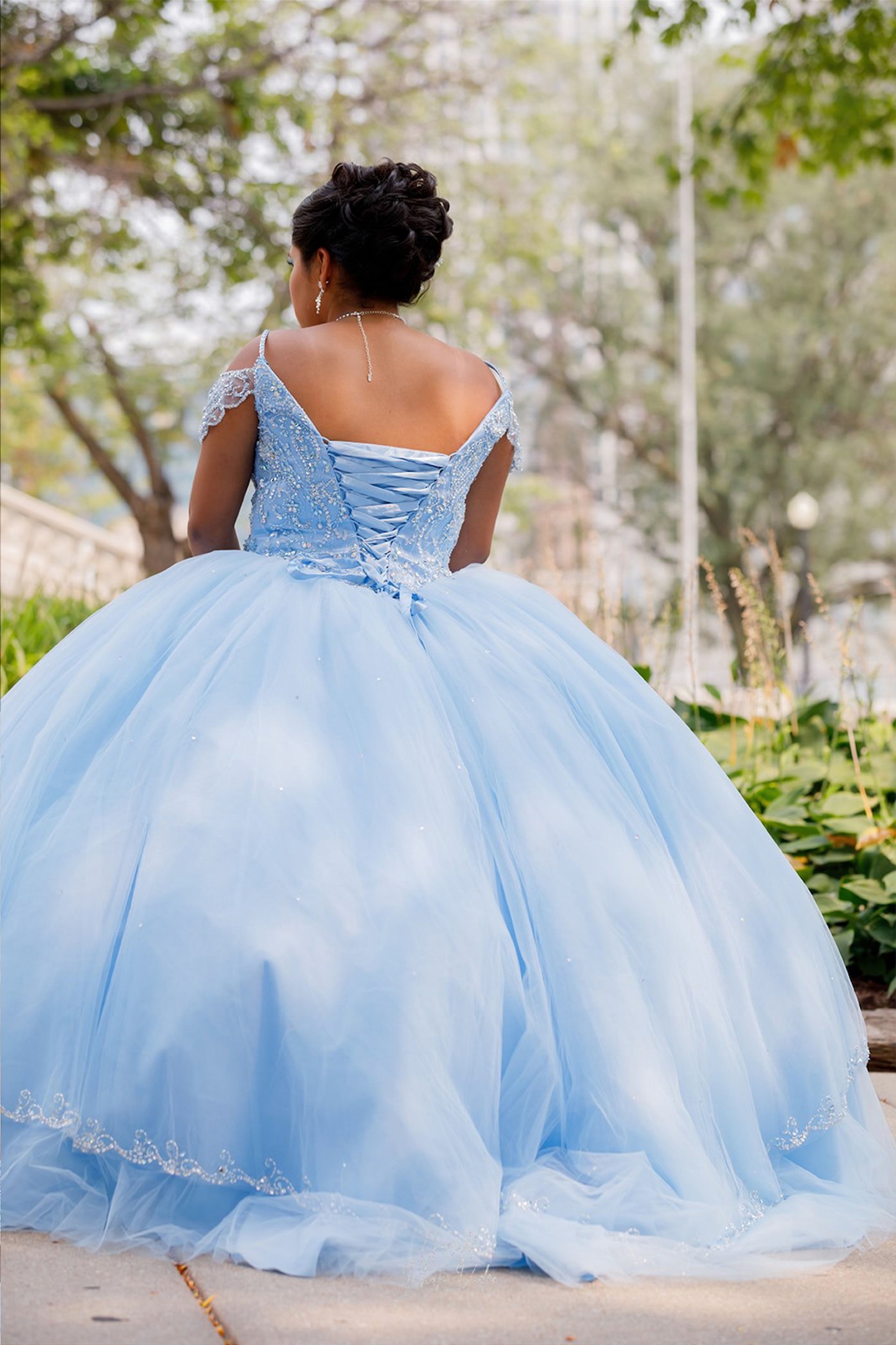 Quinceañera in a light blue ball gown seen from behind in a park, Nebraska XV años photography