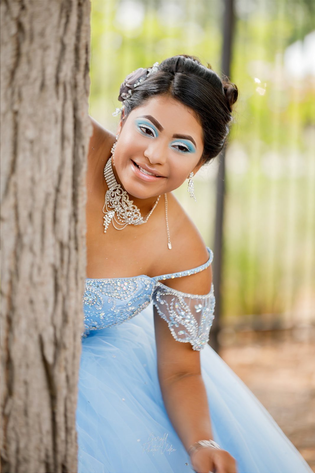 Quinceañera in a light blue gown posing beside a tree trunk, Omaha quinceañera photographer Gerald Photo Video