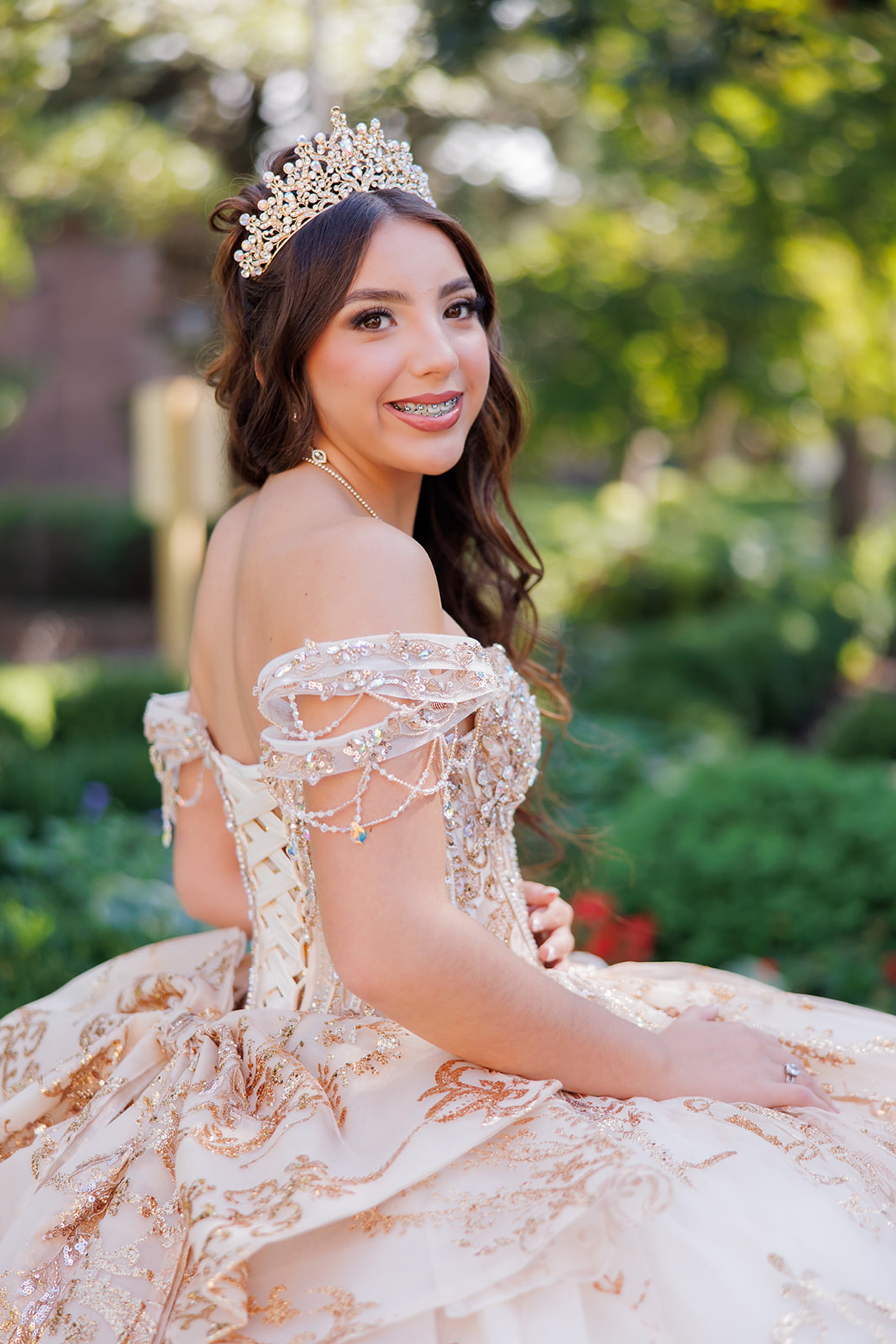 Sophia mirando sobre su hombro y sonriendo con su corona y su vestido con pedrería antes de su quinceañera en Omaha