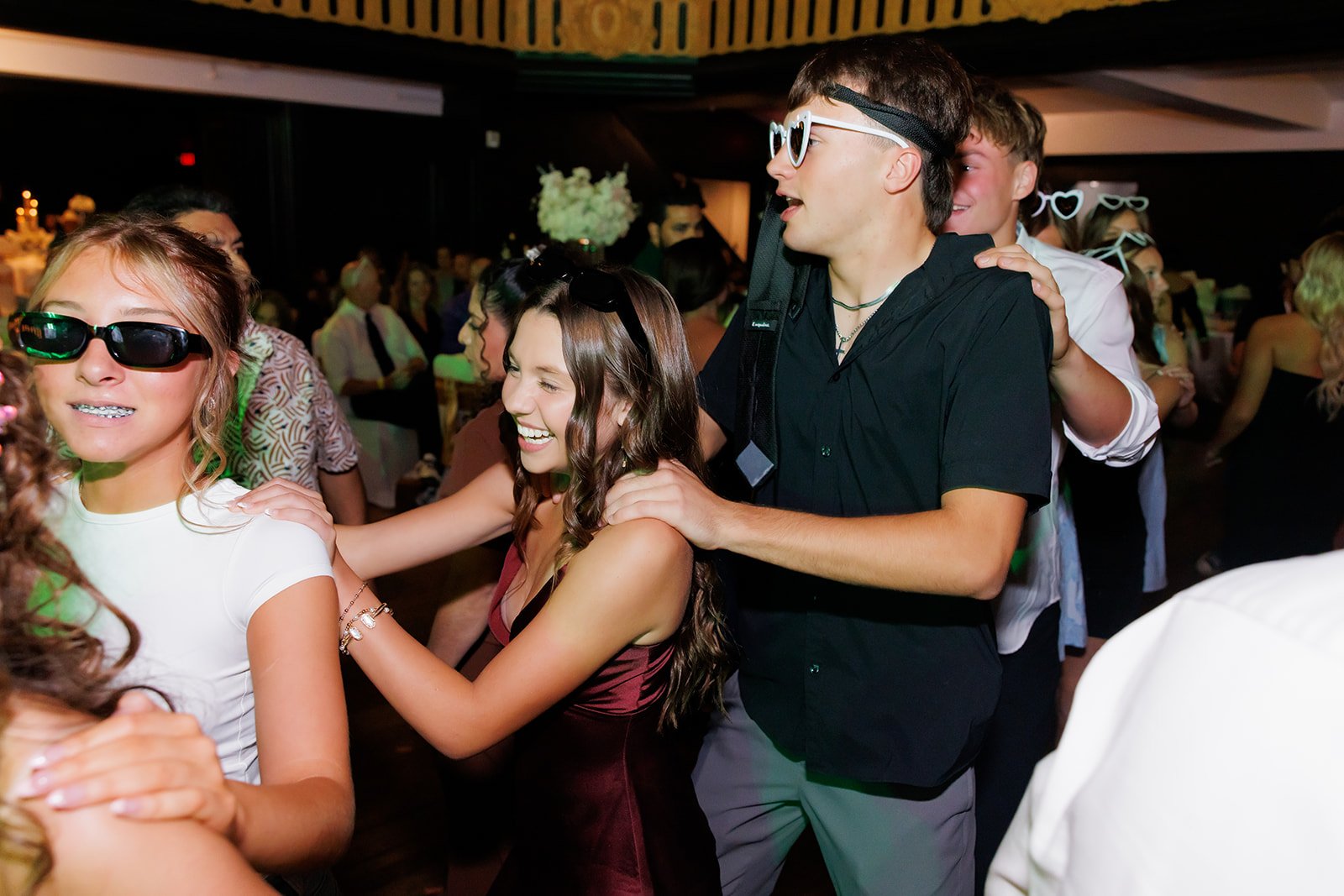 Invitados jóvenes con lentes de sol riendo y bailando en una quinceañera en Admiral Theater, Omaha