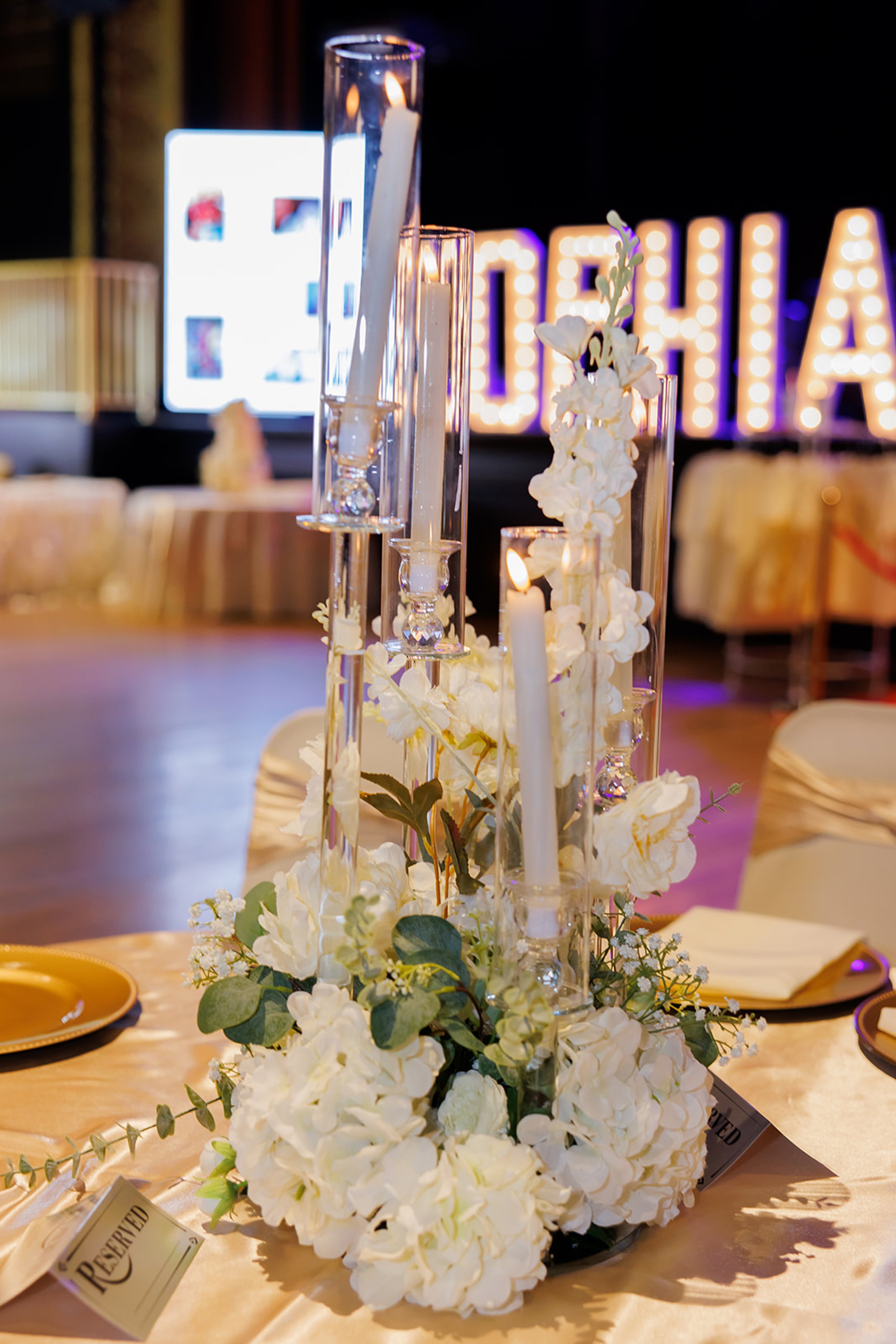 Centro de mesa de flores blancas y velas frente a un letrero iluminado con el nombre SOPHIA en su quinceañera en Omaha