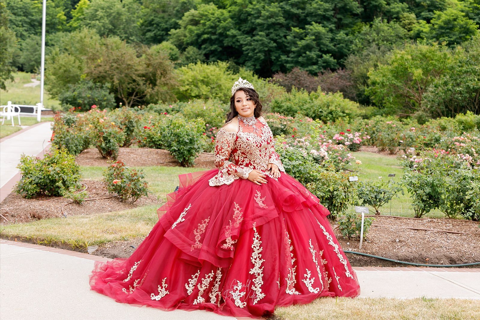 Quinceañera in a red ball gown standing in a rose garden, Nebraska XV años photography