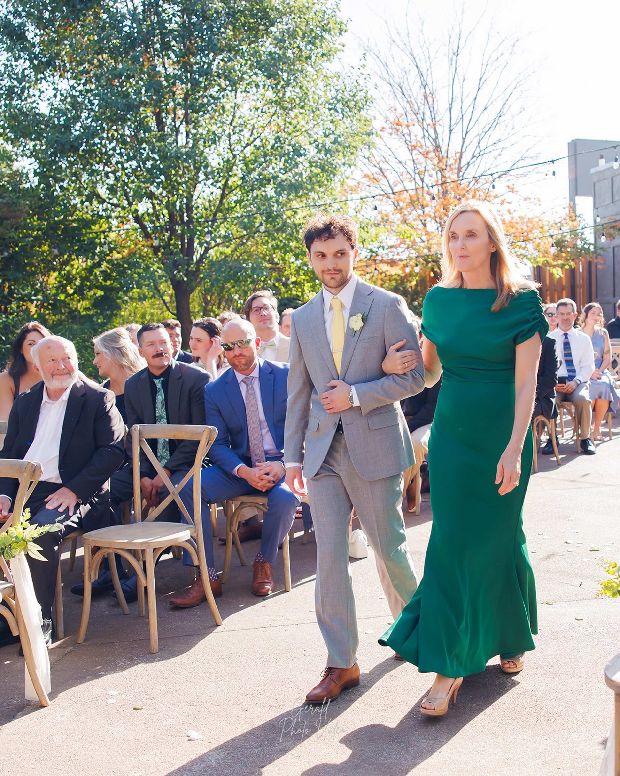 Groom walking down the aisle with his mother in an emerald green dress at The Arbor Event Venue, Omaha