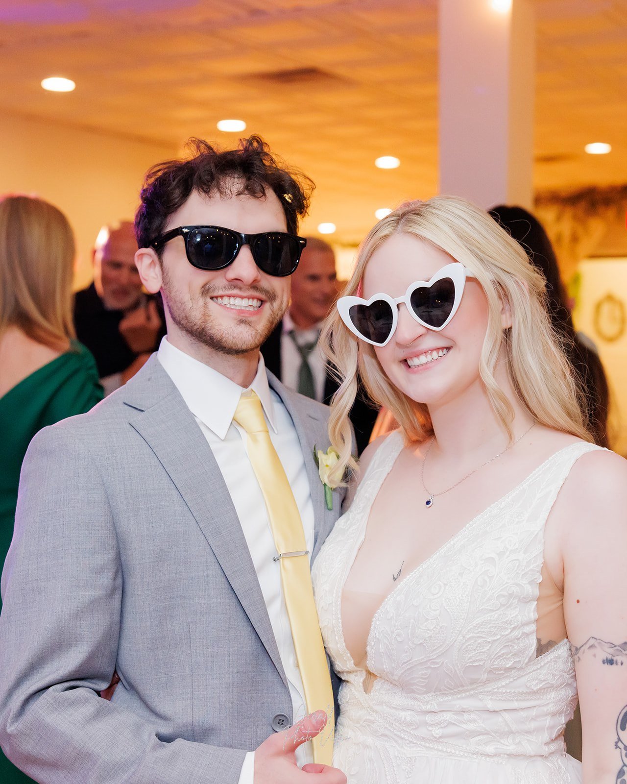 Logan and John wearing sunglasses, one pair heart shaped, having fun at their wedding reception