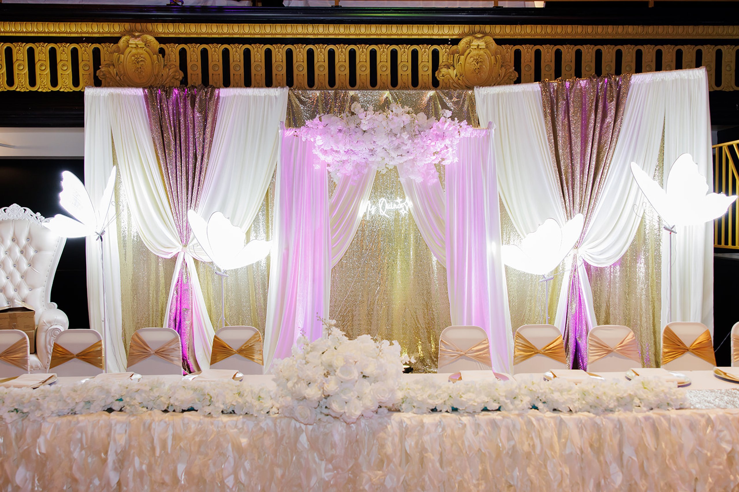Fondo de escenario con cortinas, luz suave y flores blancas en la quinceañera de Sophia en Admiral Theater, Omaha