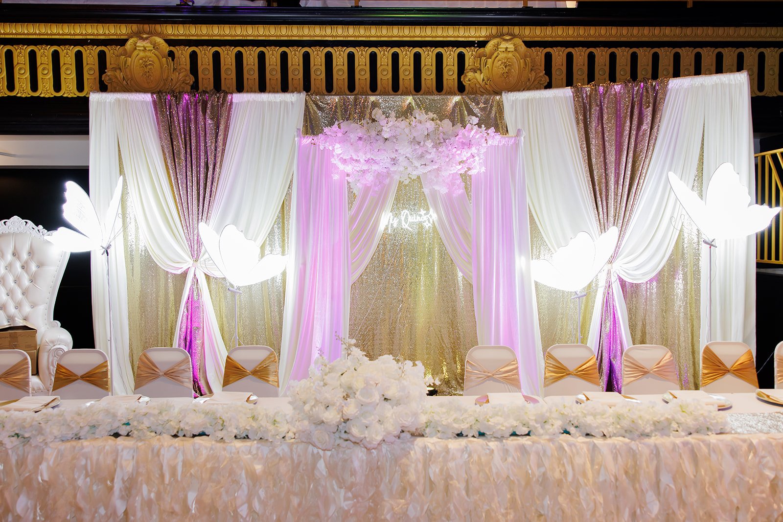 Fondo de escenario con cortinas, luz suave y flores blancas en la quinceañera de Sophia en Admiral Theater, Omaha