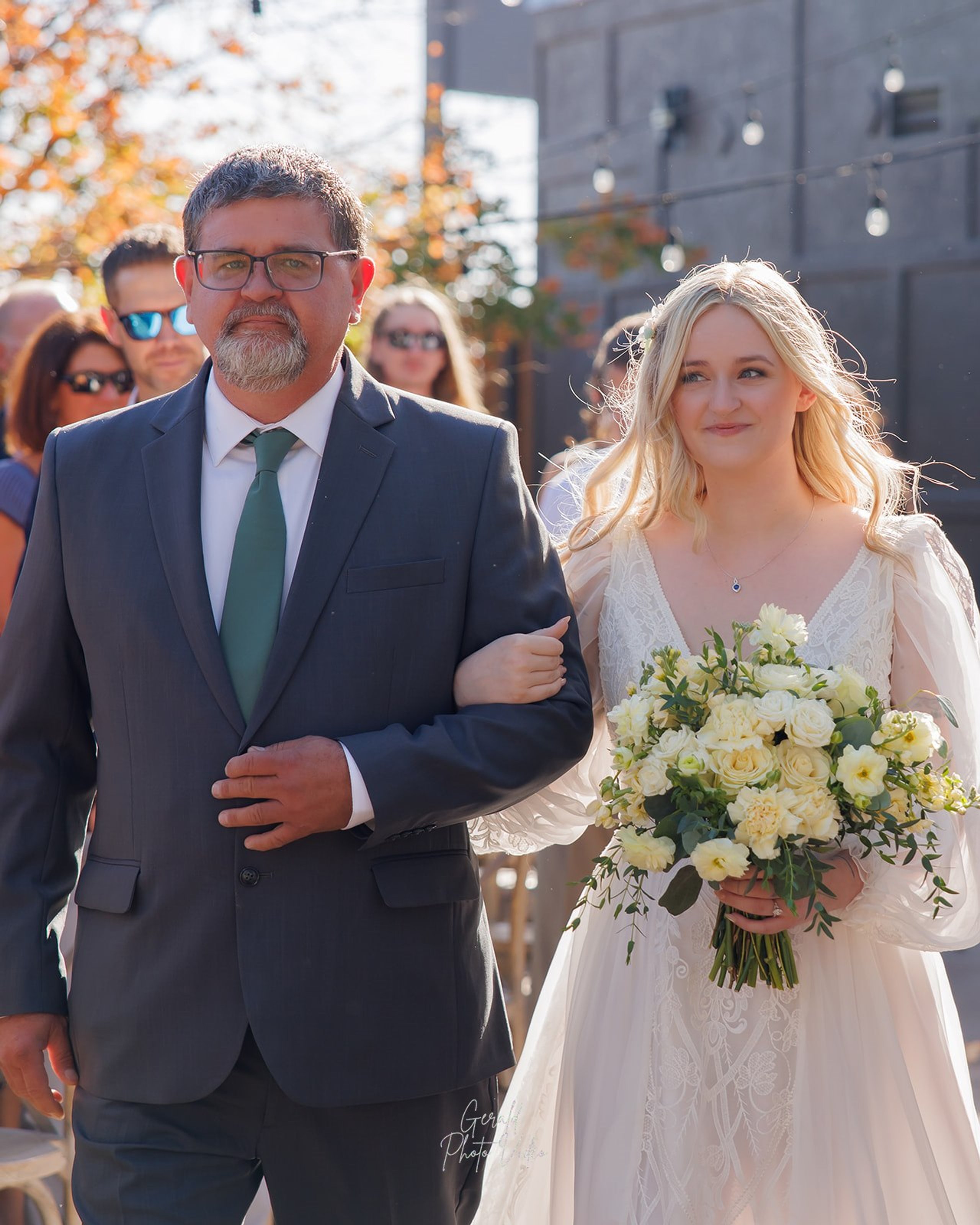Bride Logan walking down the aisle with her father at an outdoor wedding ceremony in Omaha