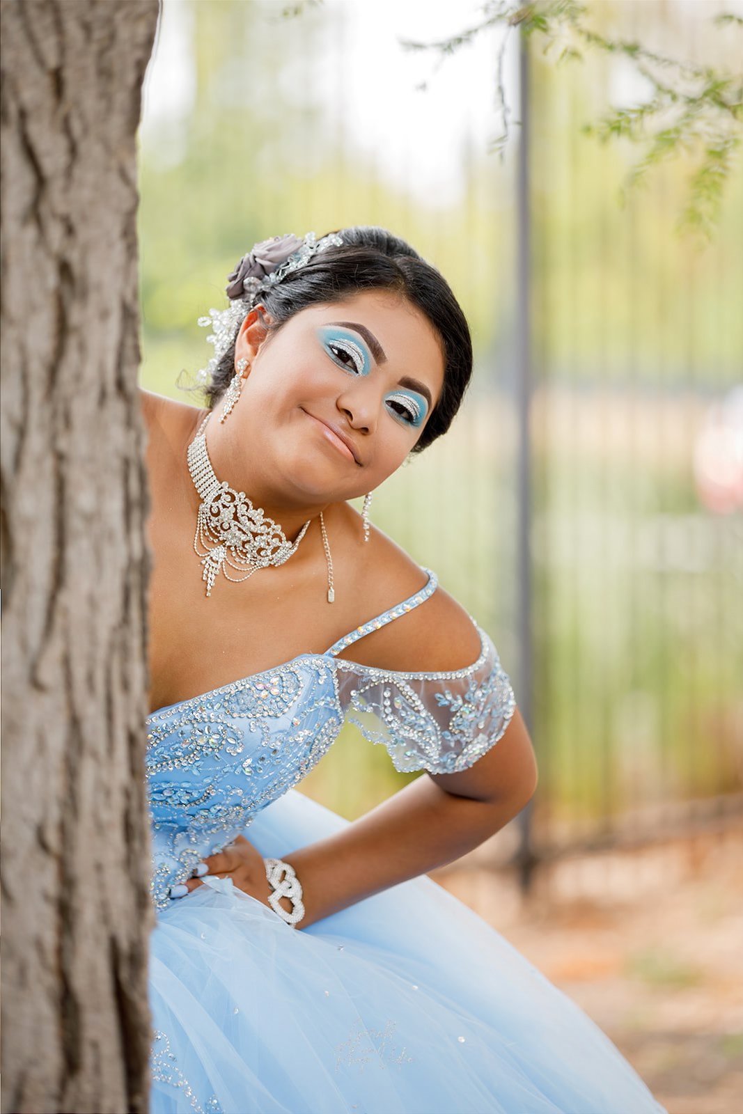 Quinceañera peeking from behind a tree in a blue off-shoulder gown, Omaha XV años photography